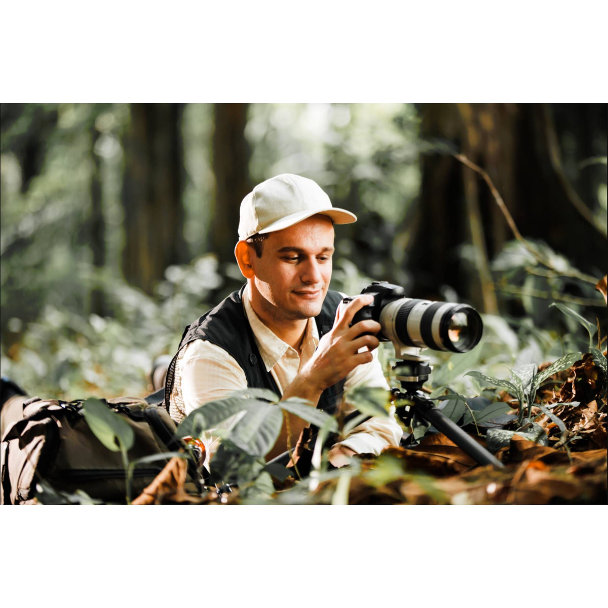 Un uomo con macchina fotografica giace in una foresta, scattando una foto.
