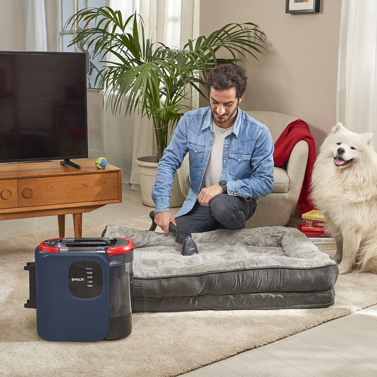 Uomo pulisce cuccia con macchina, cane seduto accanto.