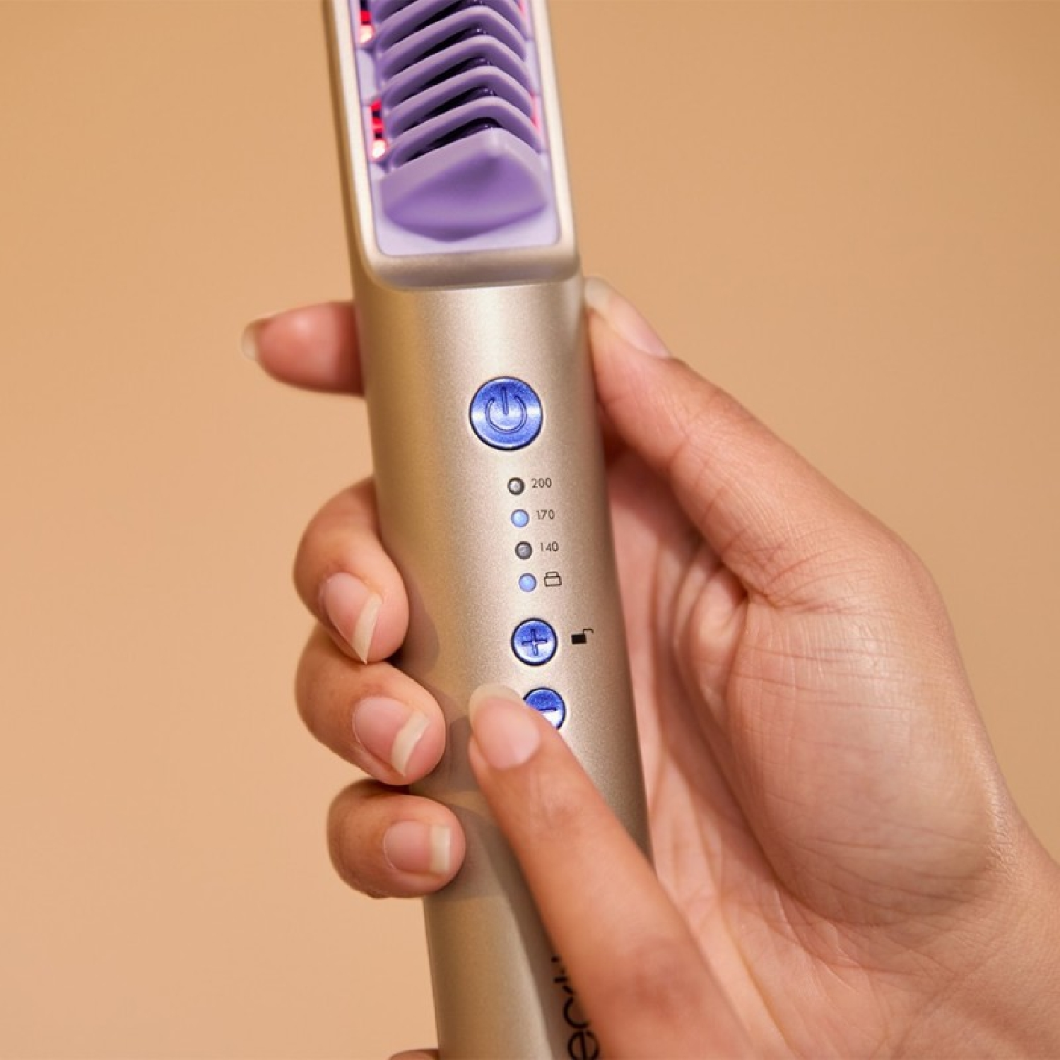 Una mano sostiene un peine dorado para alisar el cabello con cerdas moradas y botones azules.