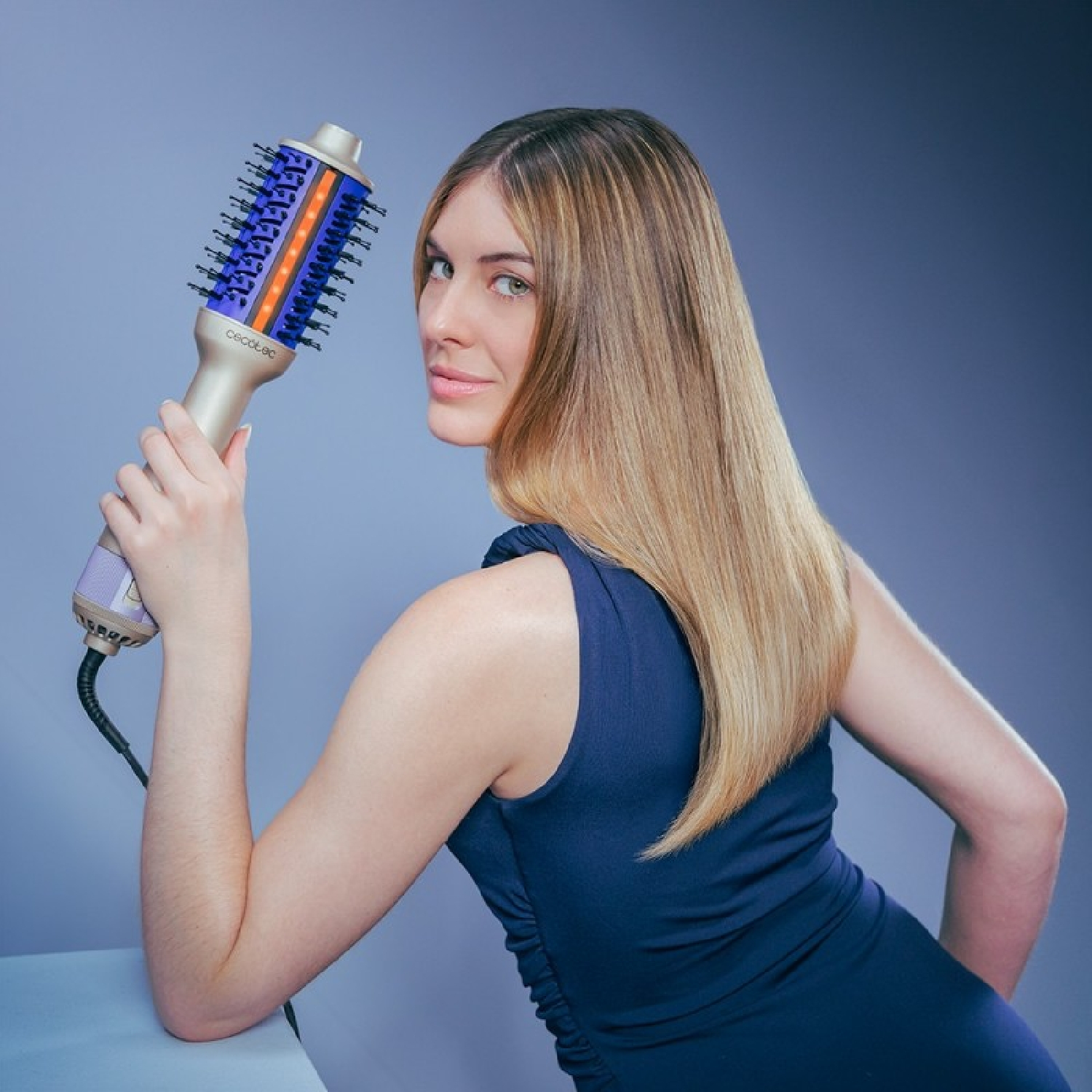 Una mujer rubia sostiene un secador de pelo azul y morado.