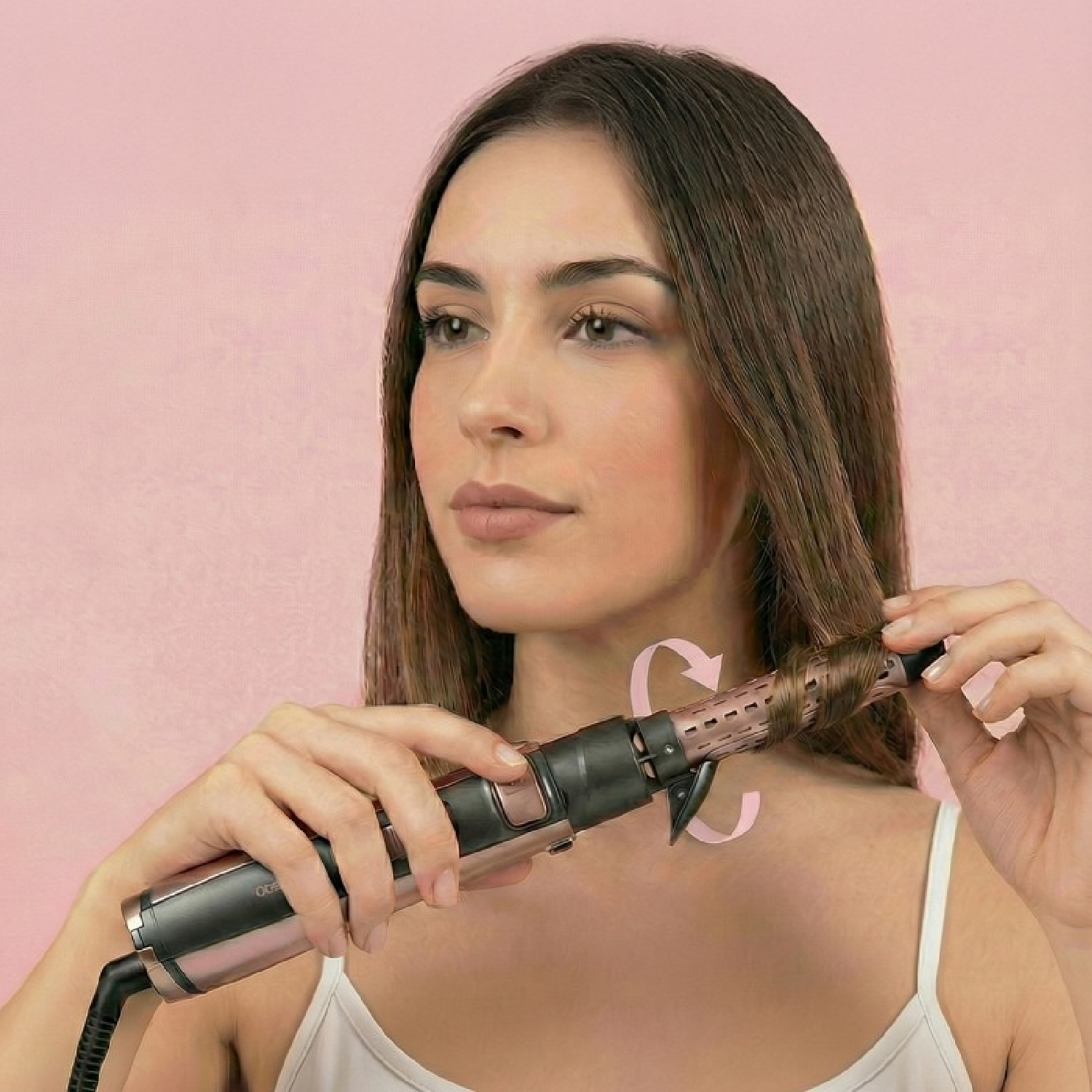 Una mujer con cabello castaño usa un rizador automático sobre fondo rosa.