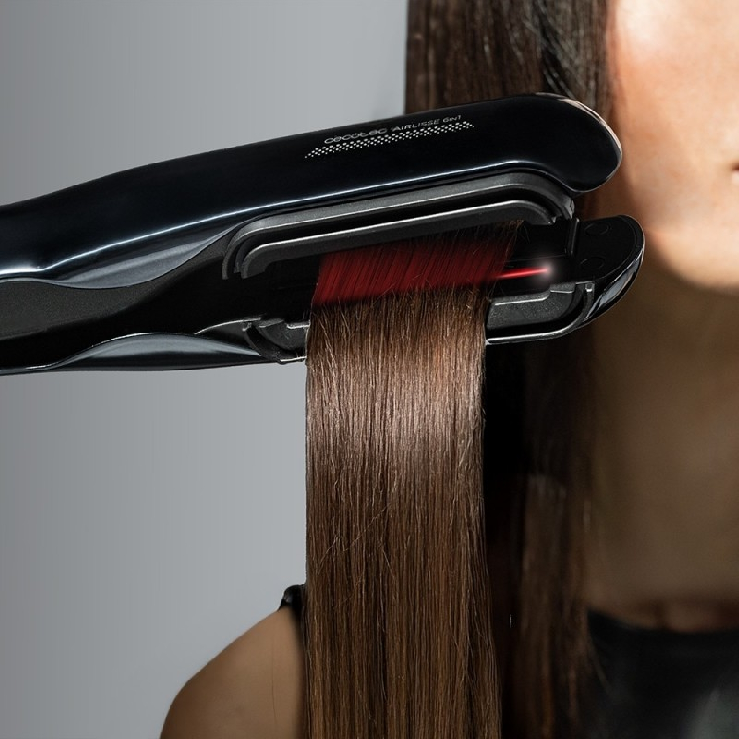 Piastra per capelli nera che liscia capelli castani con raggio di luce rossa.