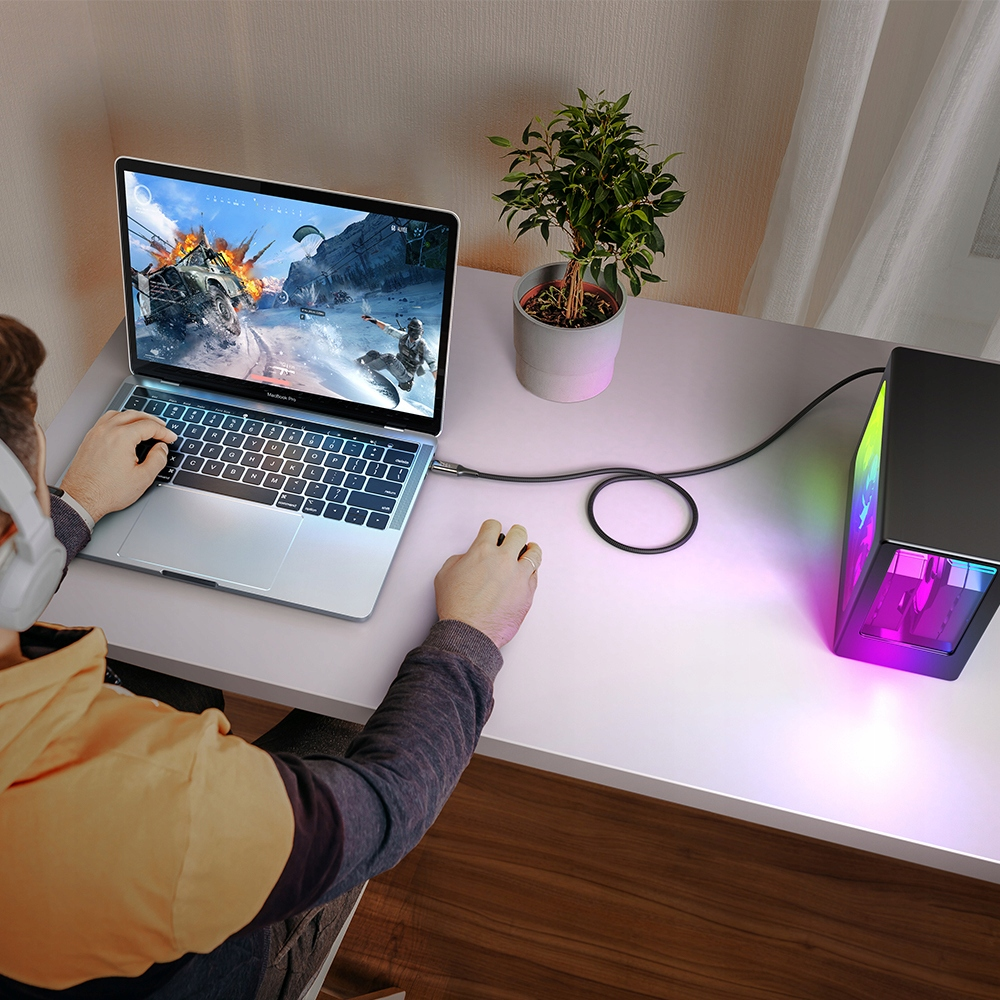 Kişi, renkli bir PC kasasına bağlı dizüstü bilgisayarda video oyunu oynuyor.