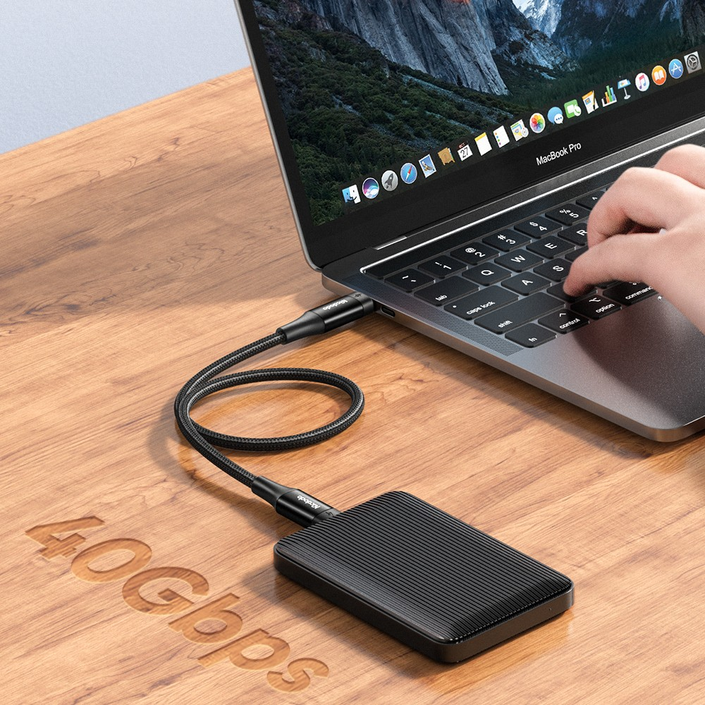 Siyah harici sabit disk, ahşap bir masada örgülü kablo ile MacBook Pro'ya bağlanır.