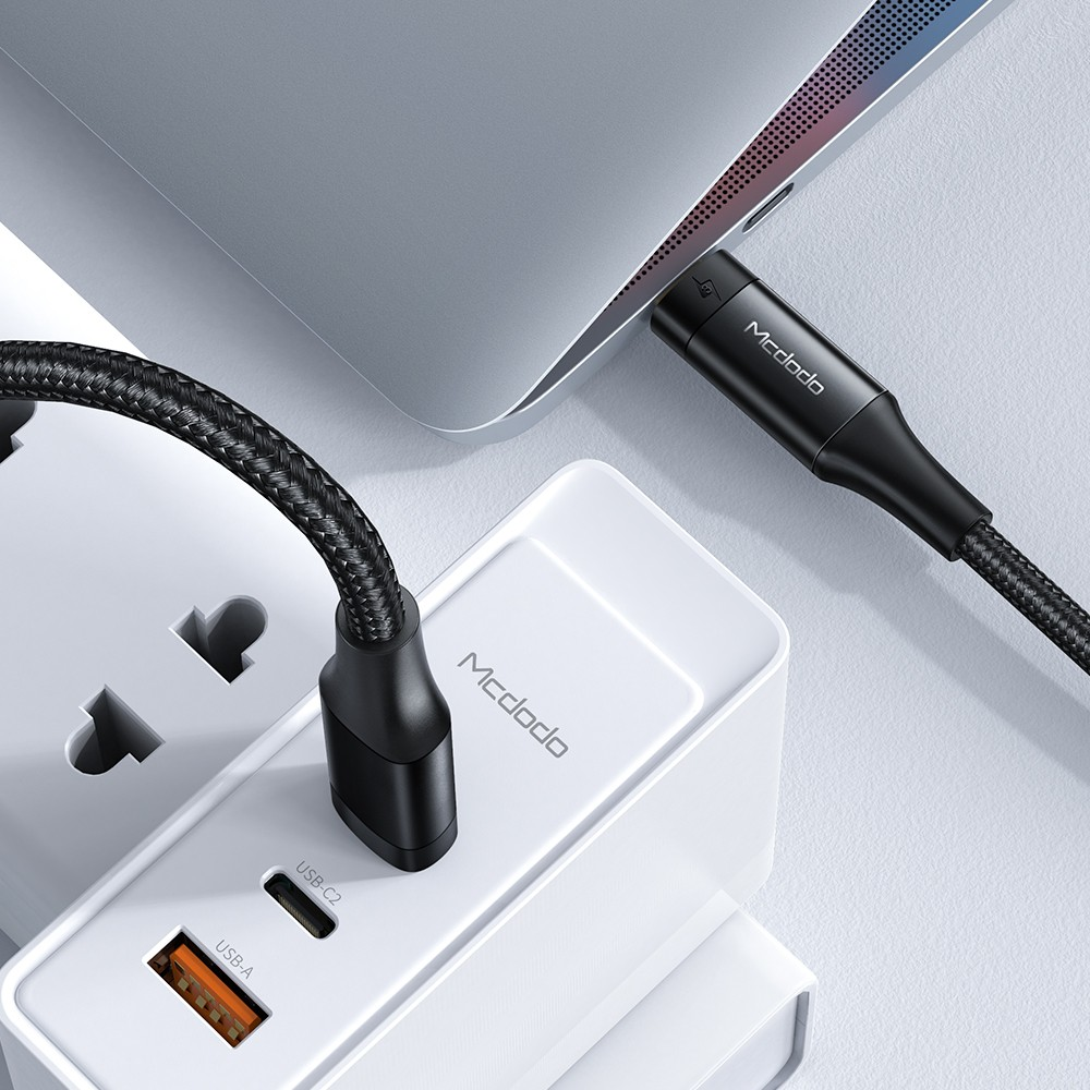 Siyah bir USB-C kablosu, beyaz bir güç adaptörüne bağlı bir dizüstü bilgisayarı şarj ediyor.