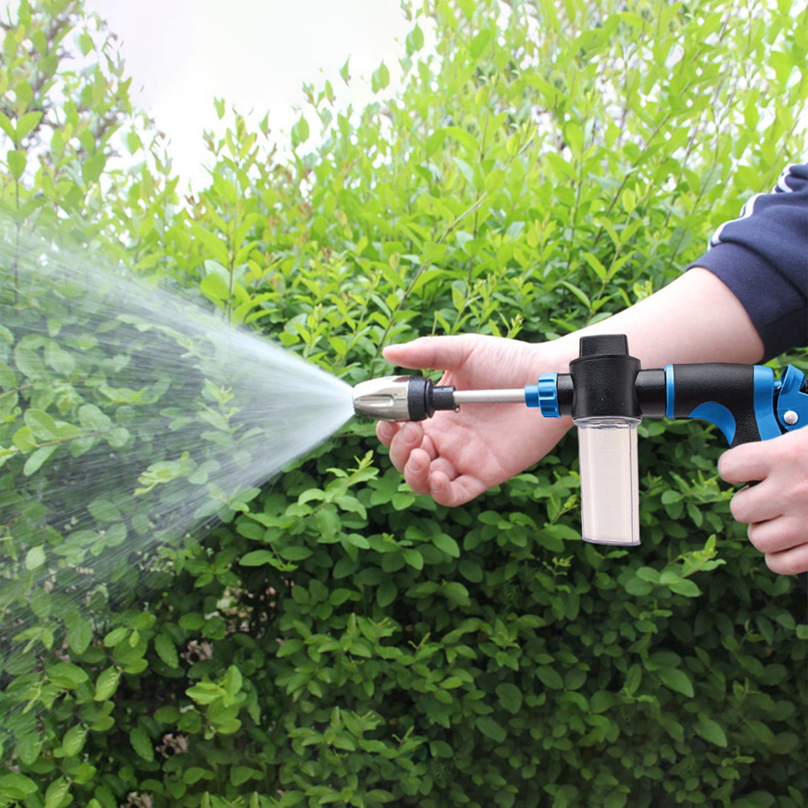 Eine Hand hält eine Spritzpistole, die Wasser auf einen grünen Busch sprüht.