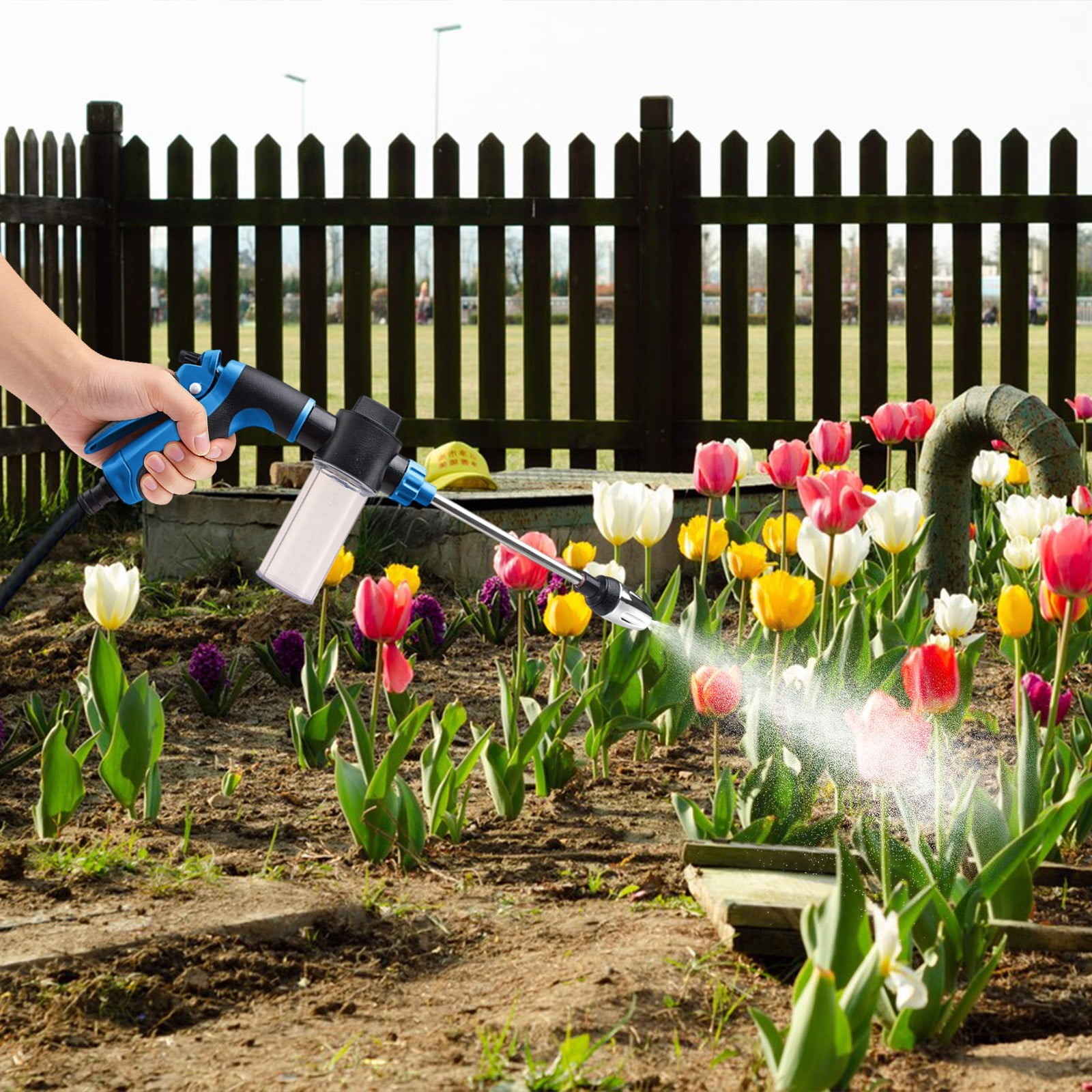 Eine Hand hält eine blaue Spritzpistole mit einem Behälter, die Blumen besprüht.