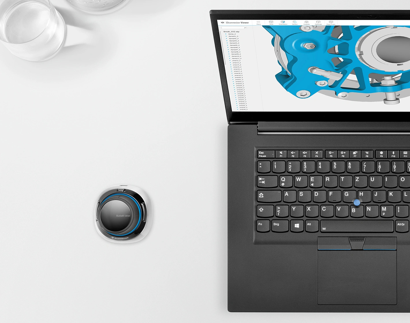 Een laptop toont een 3D-model, ernaast een 3D-muiscontroller en glazen.