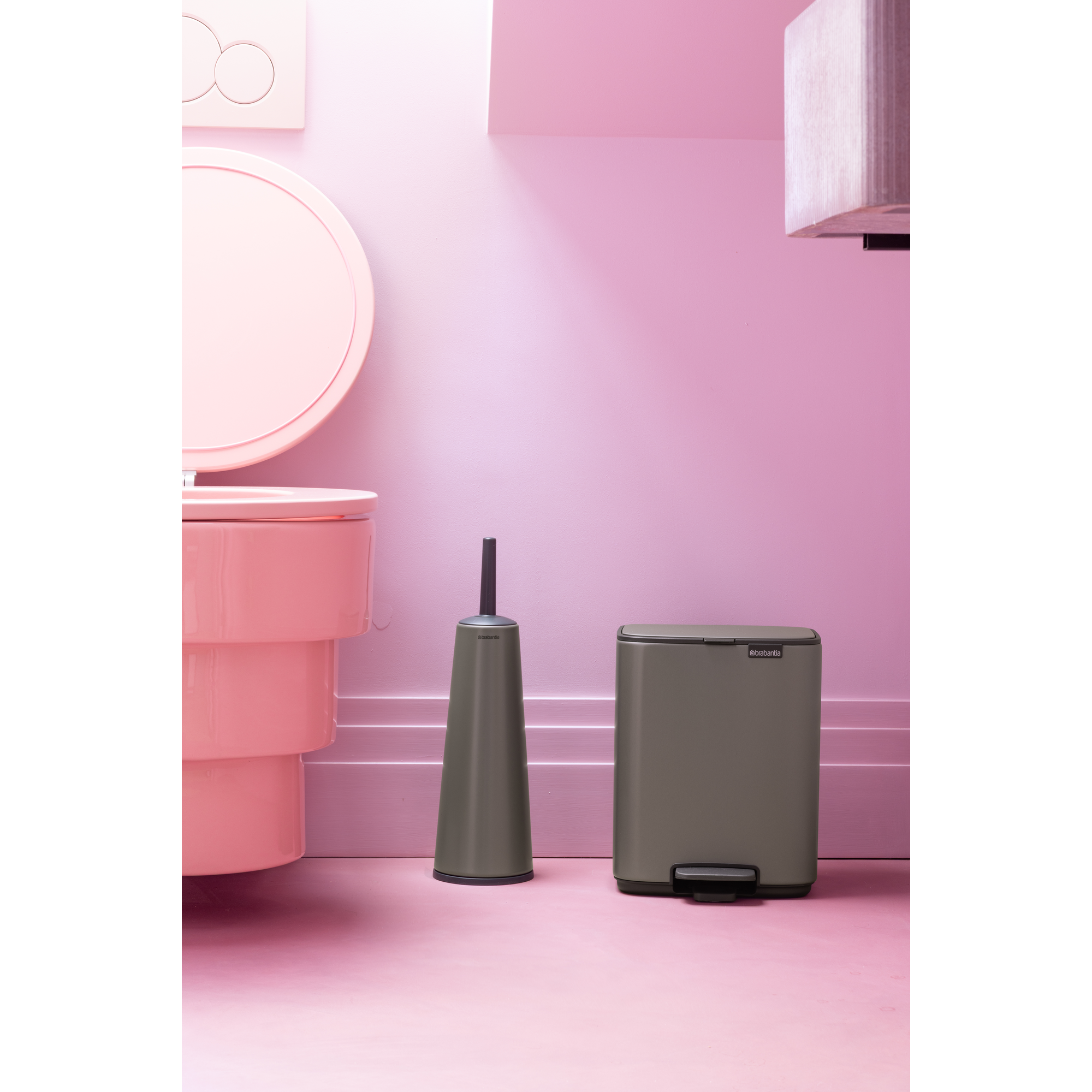 Een roze toilet met borstel en prullenbak op roze vloer.