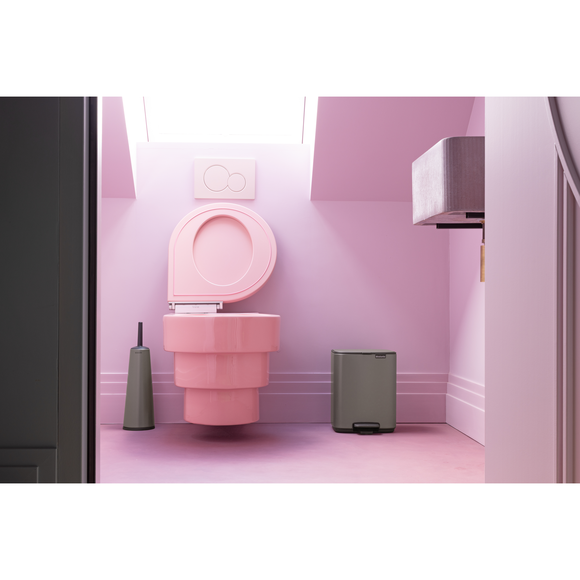 Een roze toilet met borstel en prullenbak in een pastelkleurige kamer.