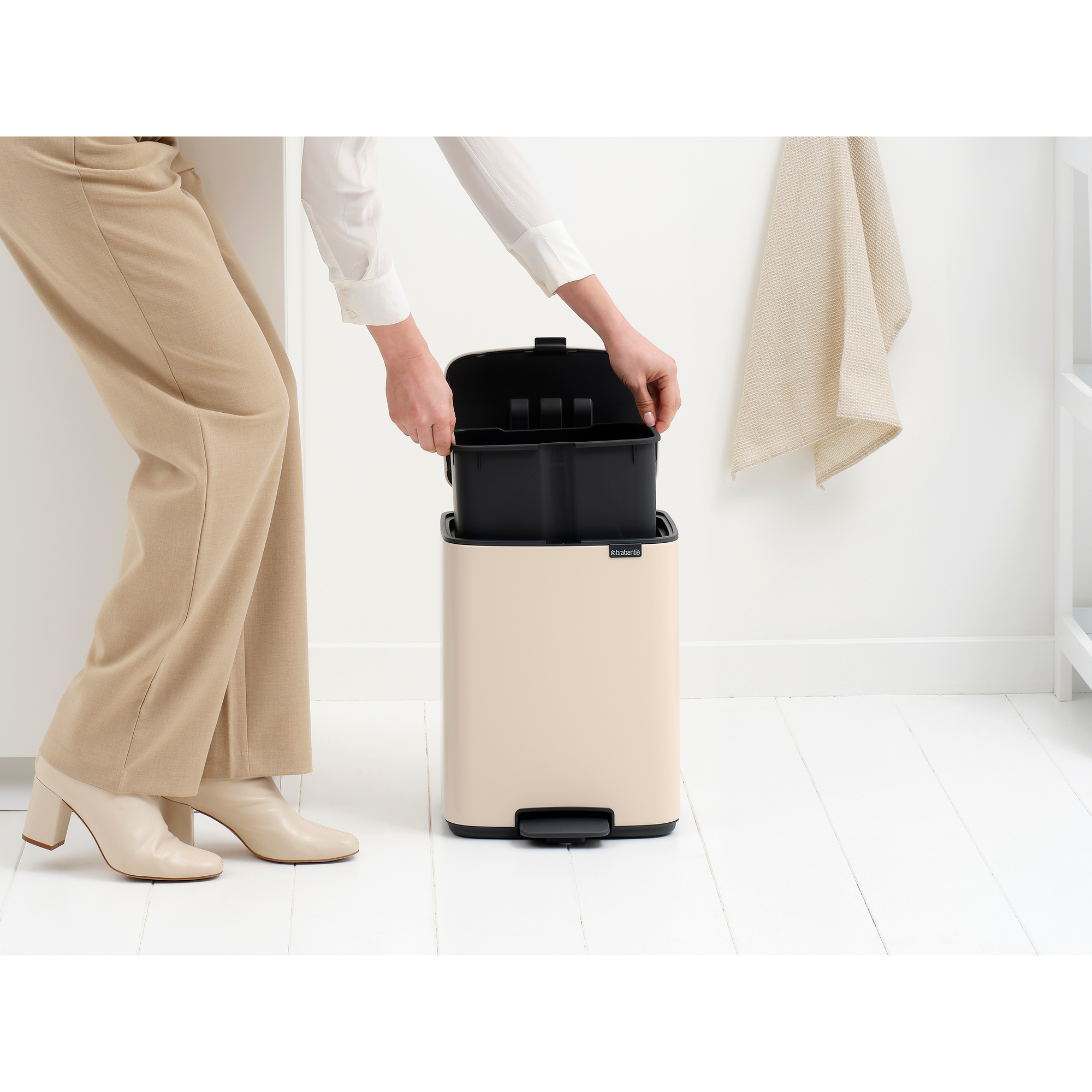 Een persoon in beige broek en wit shirt plaatst een zwarte vuilnisbak-inzet.