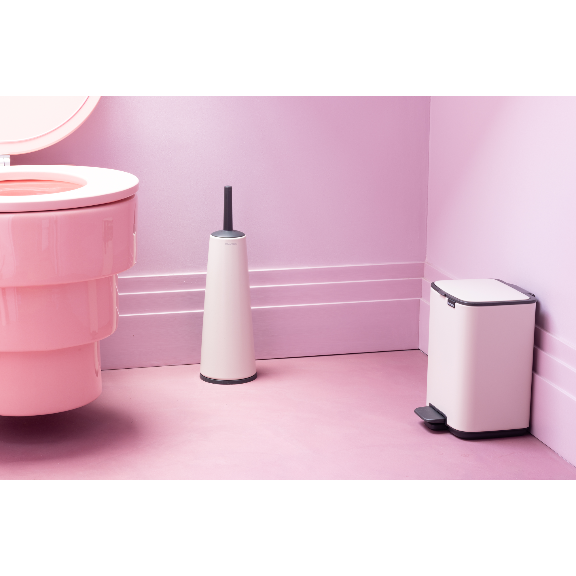 Een roze toilet, witte borstel en witte prullenbak op roze vloer.