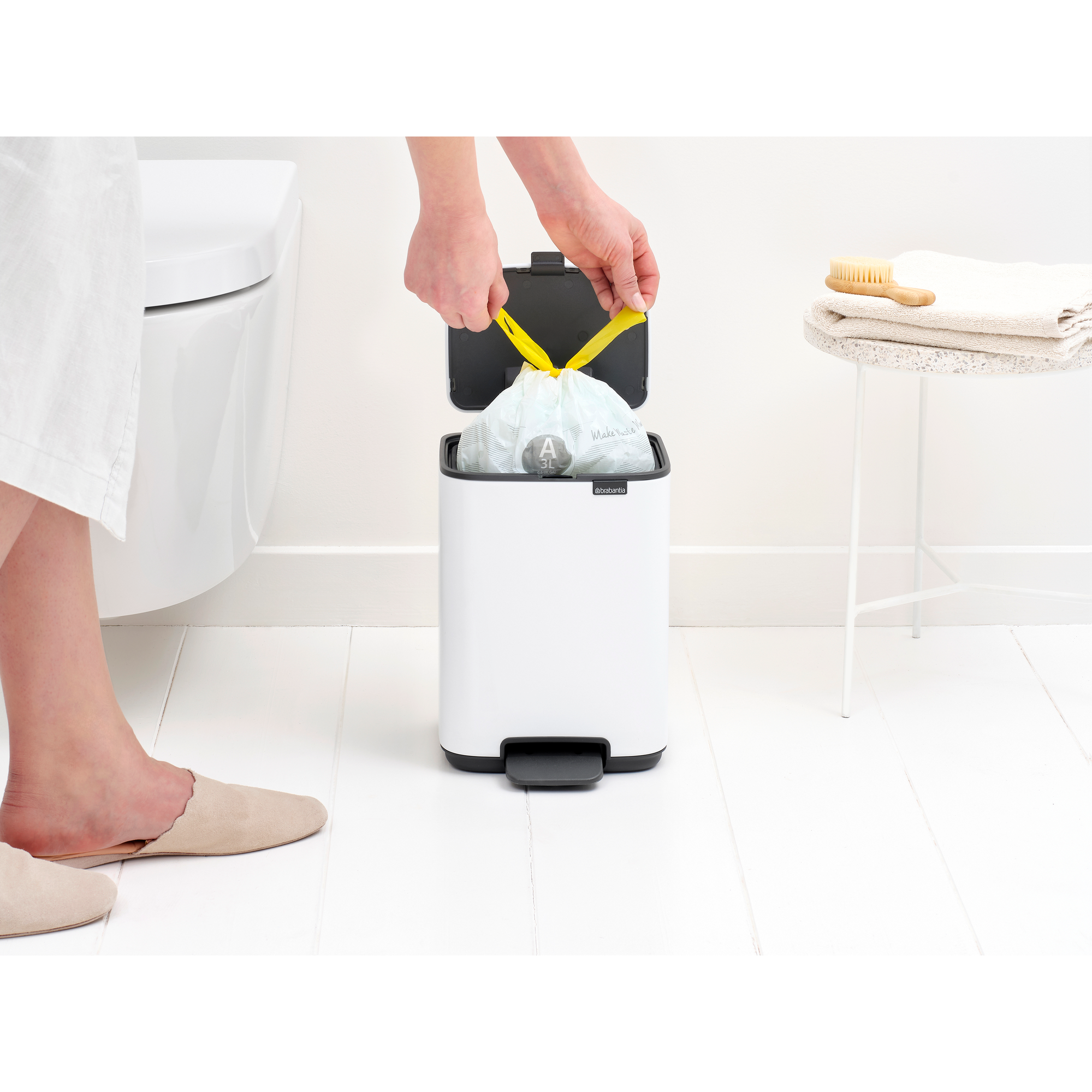 Handen trekken een gele zak uit een witte prullenbak naast toilet.