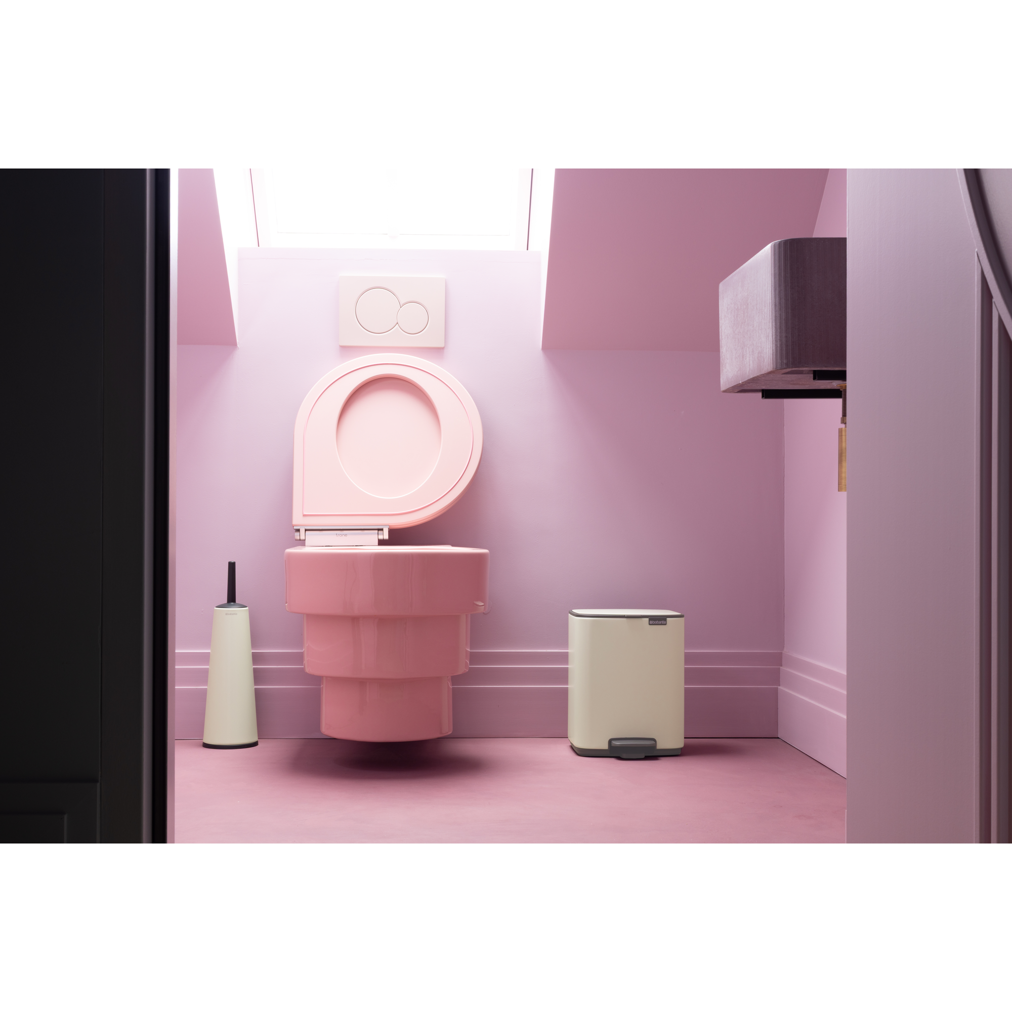 Een roze badkamer met toilet, borstel en prullenbak.