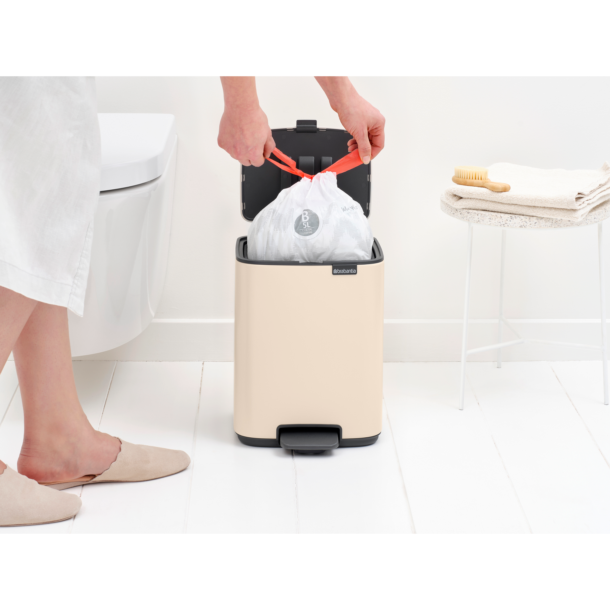 Een persoon verwisselt een vuilniszak in een badkamer met toilet.