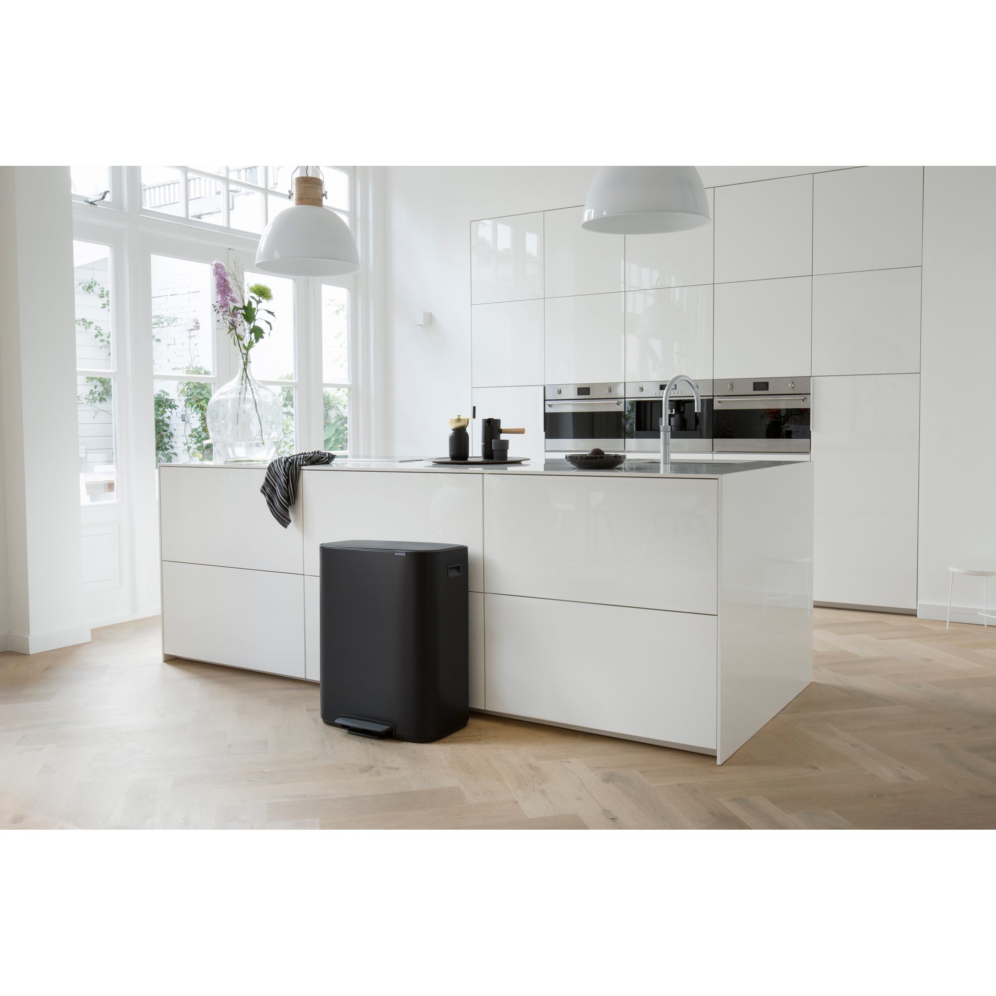 Moderne witte keuken met eiland, prullenbak en groot raam.