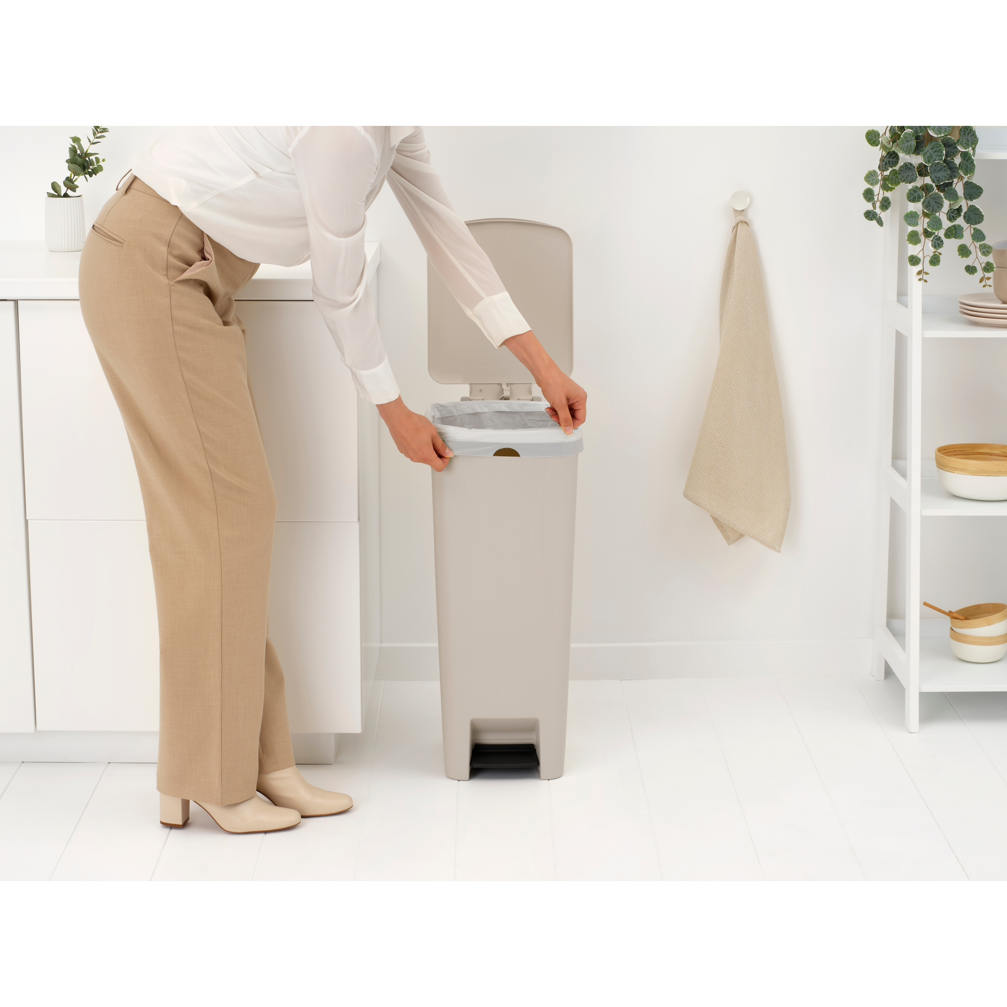 A person in beige pants and a white shirt places a liner in a beige trash can.