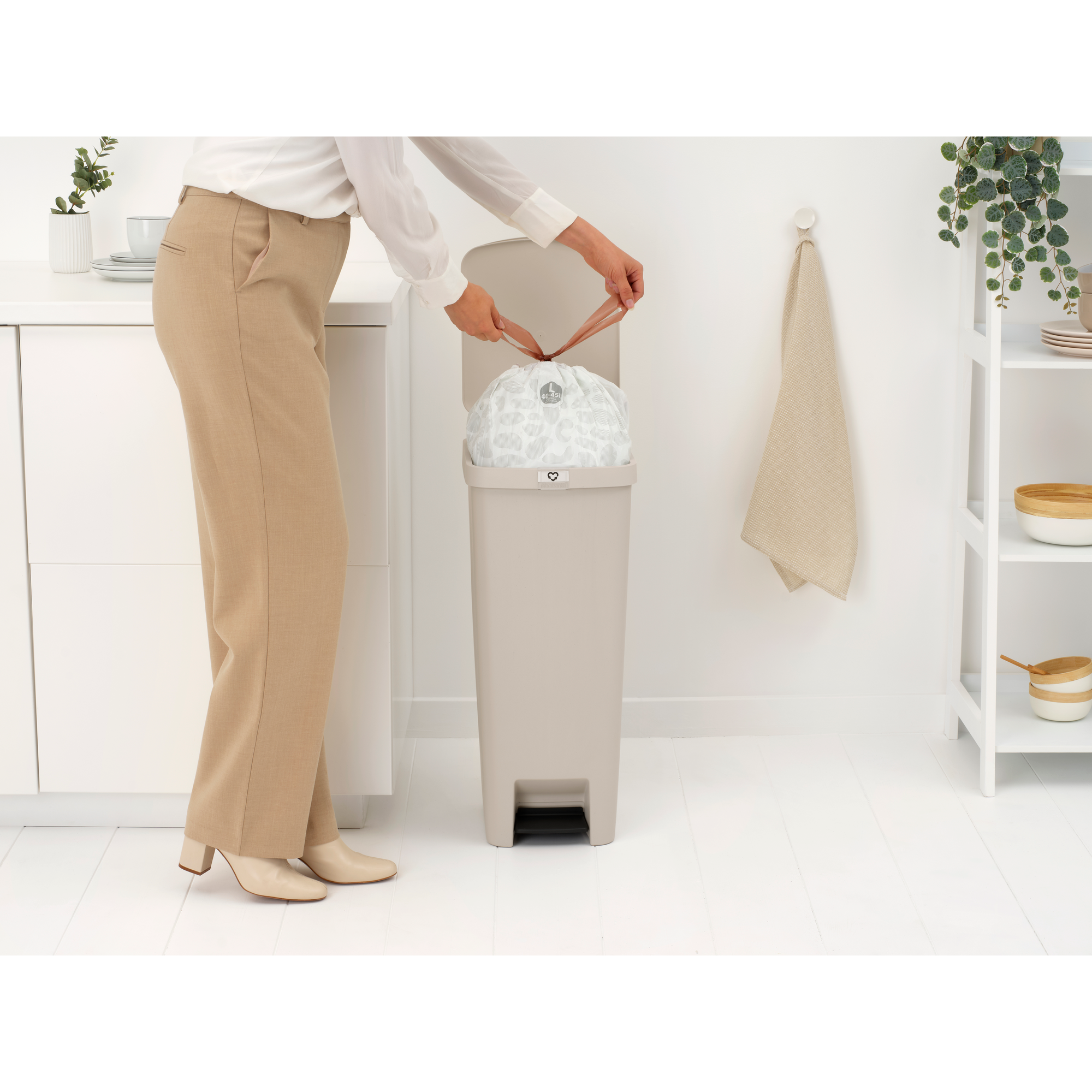 A woman ties a trash bag in a beige trash can.