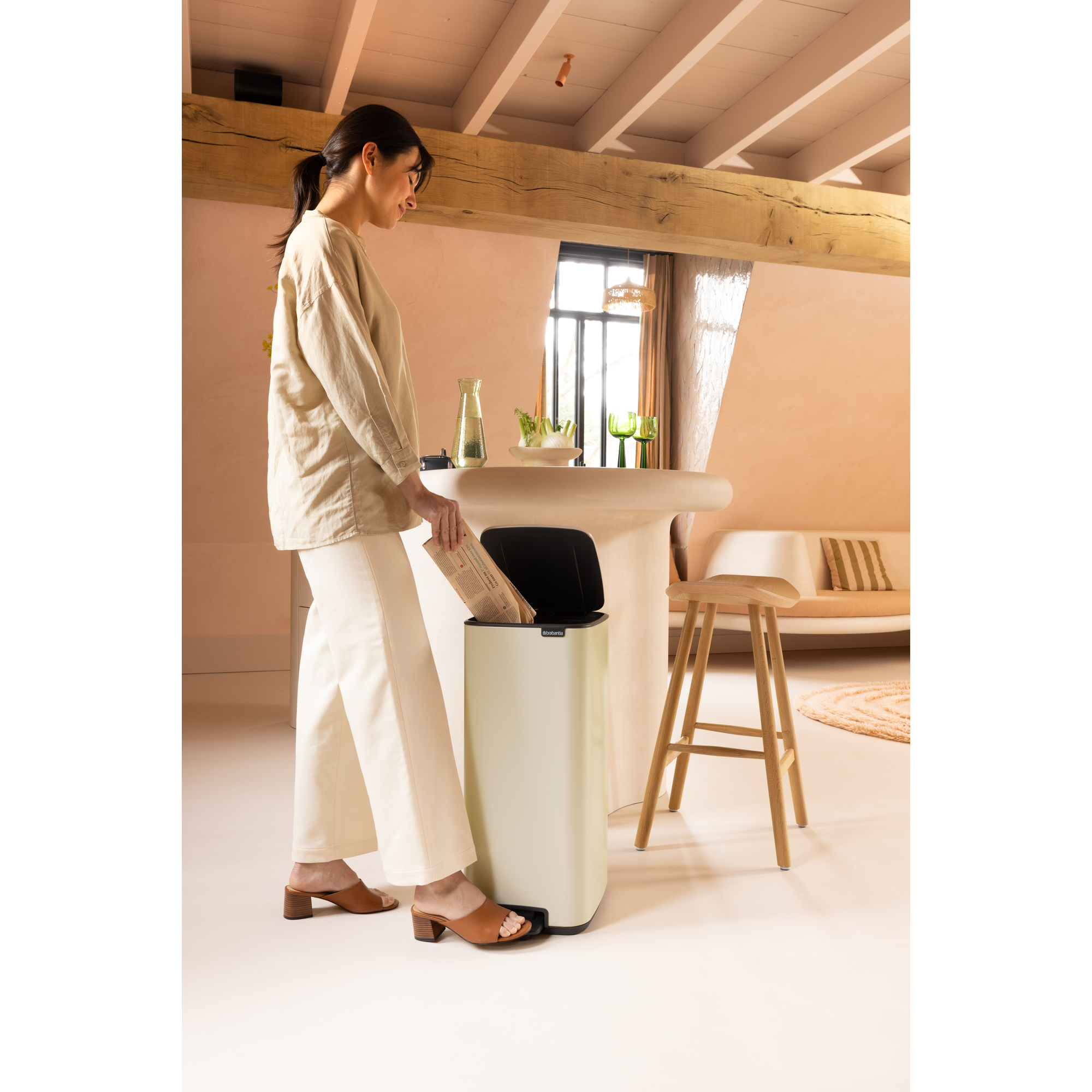 Een vrouw gooit kranten in een lichtbeige pedaalemmer in een stijlvolle keuken.