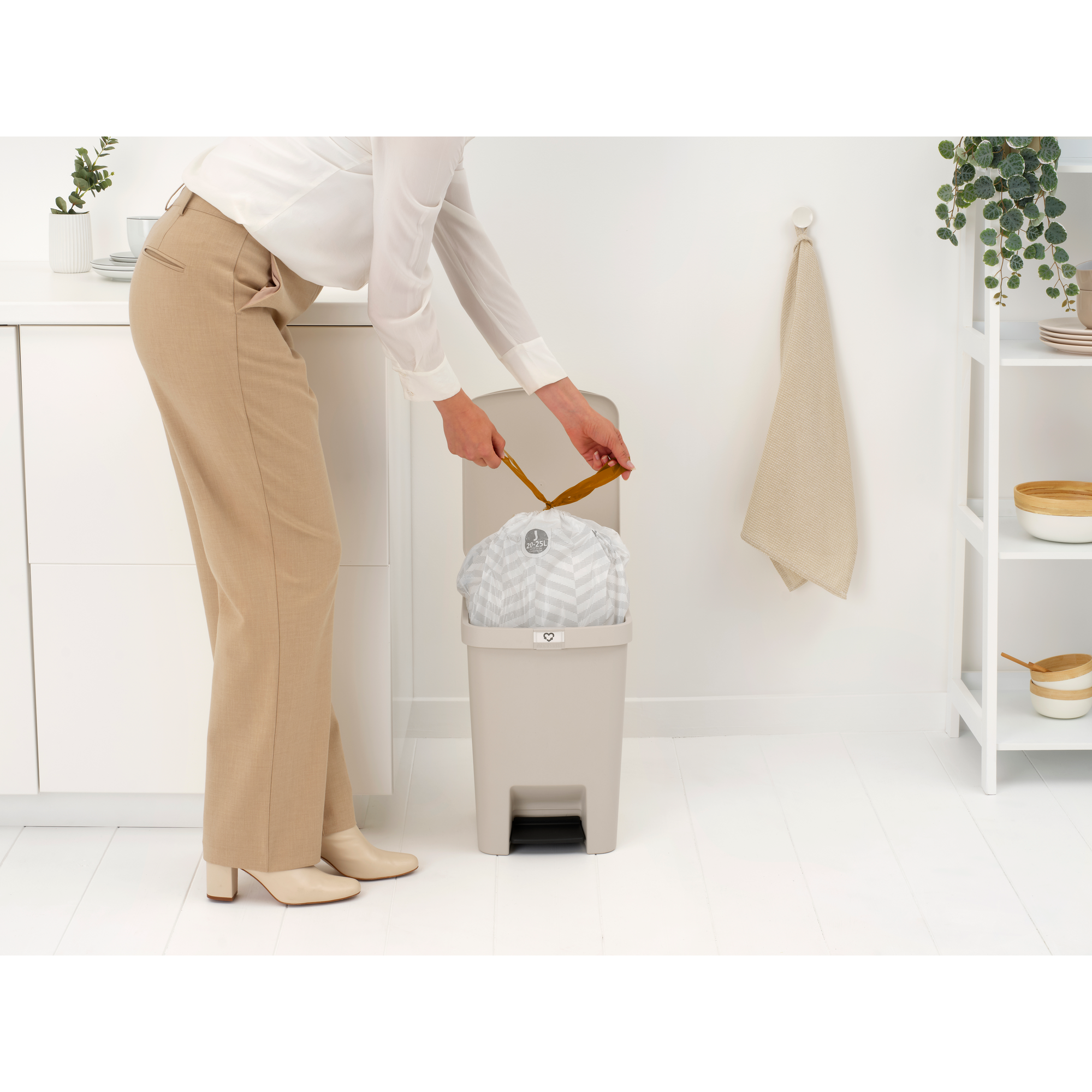 Een vrouw sluit een vuilniszak in een beige prullenbak.