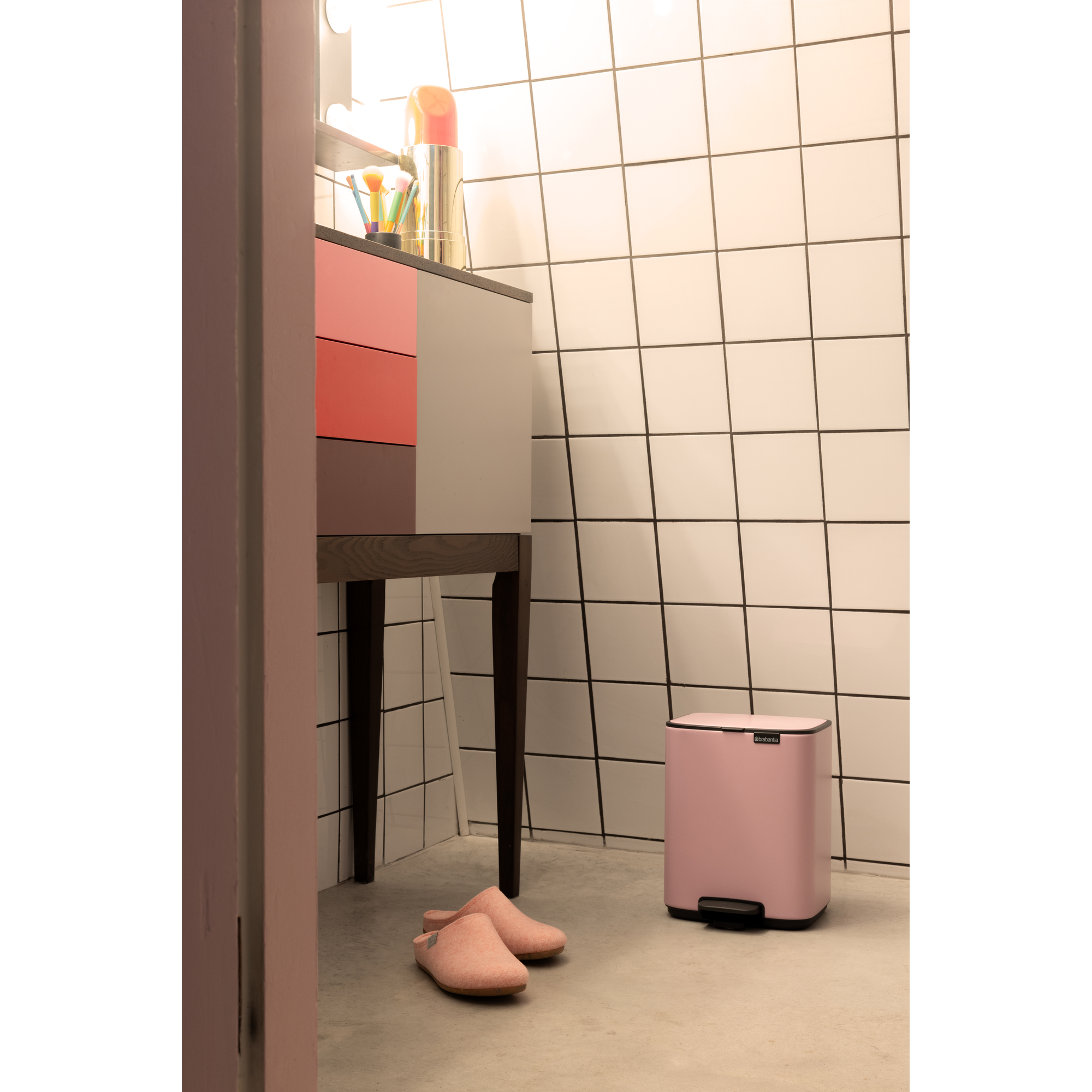 Een roze prullenbak naast een kast met make-upkwasten.