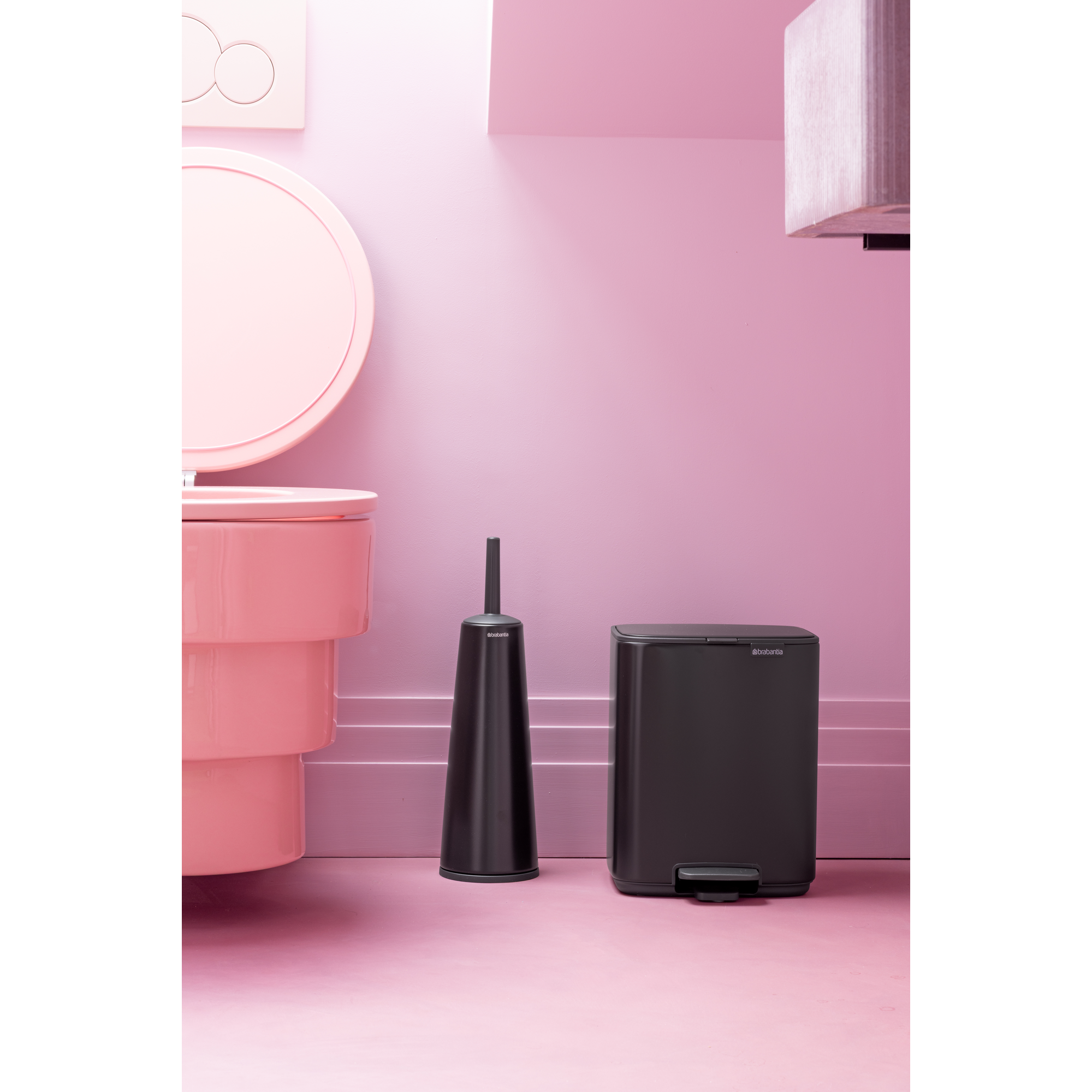 A pink toilet and a black trash can stand on a pink floor.