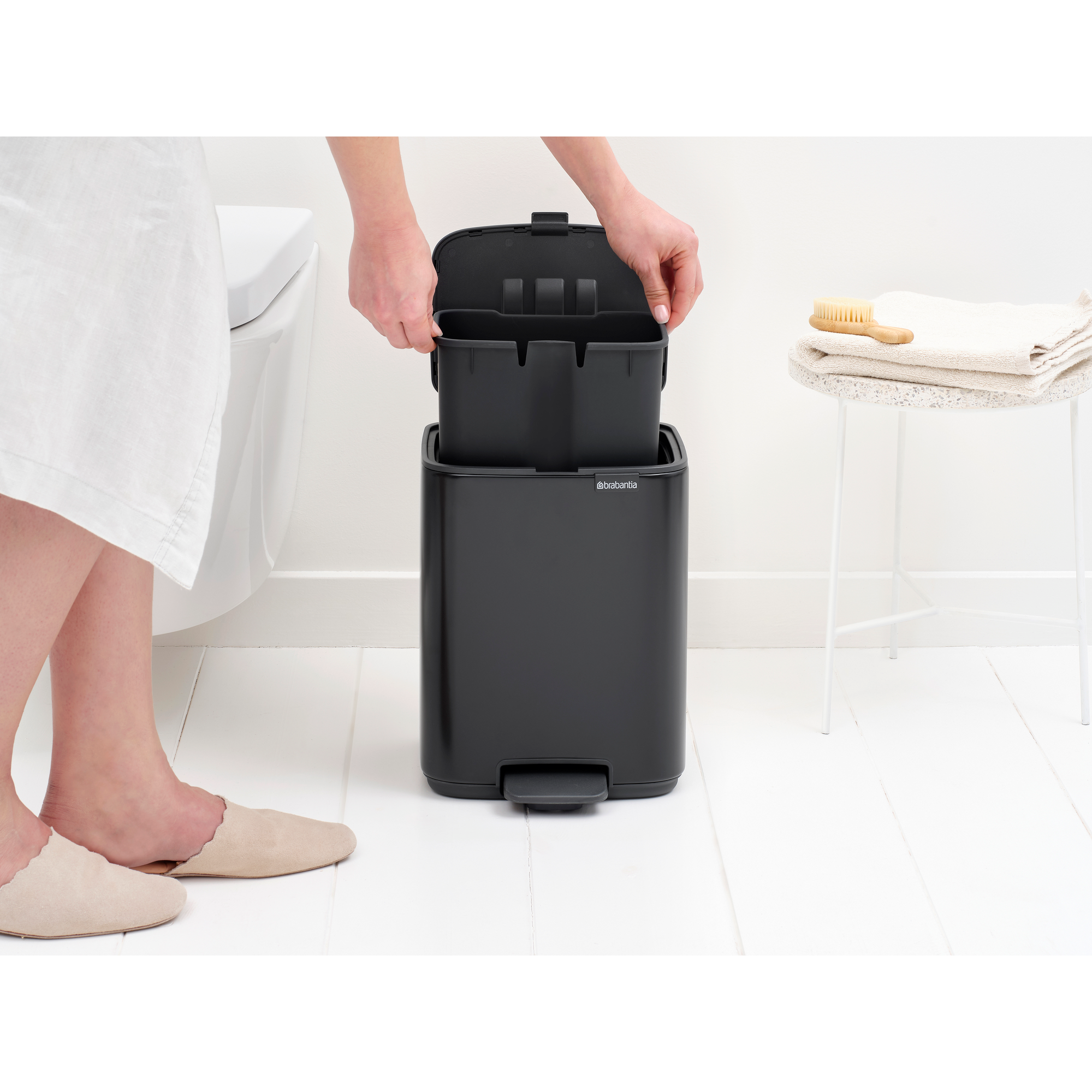 Person inserts a bin liner; a stool with towel and brush is nearby.