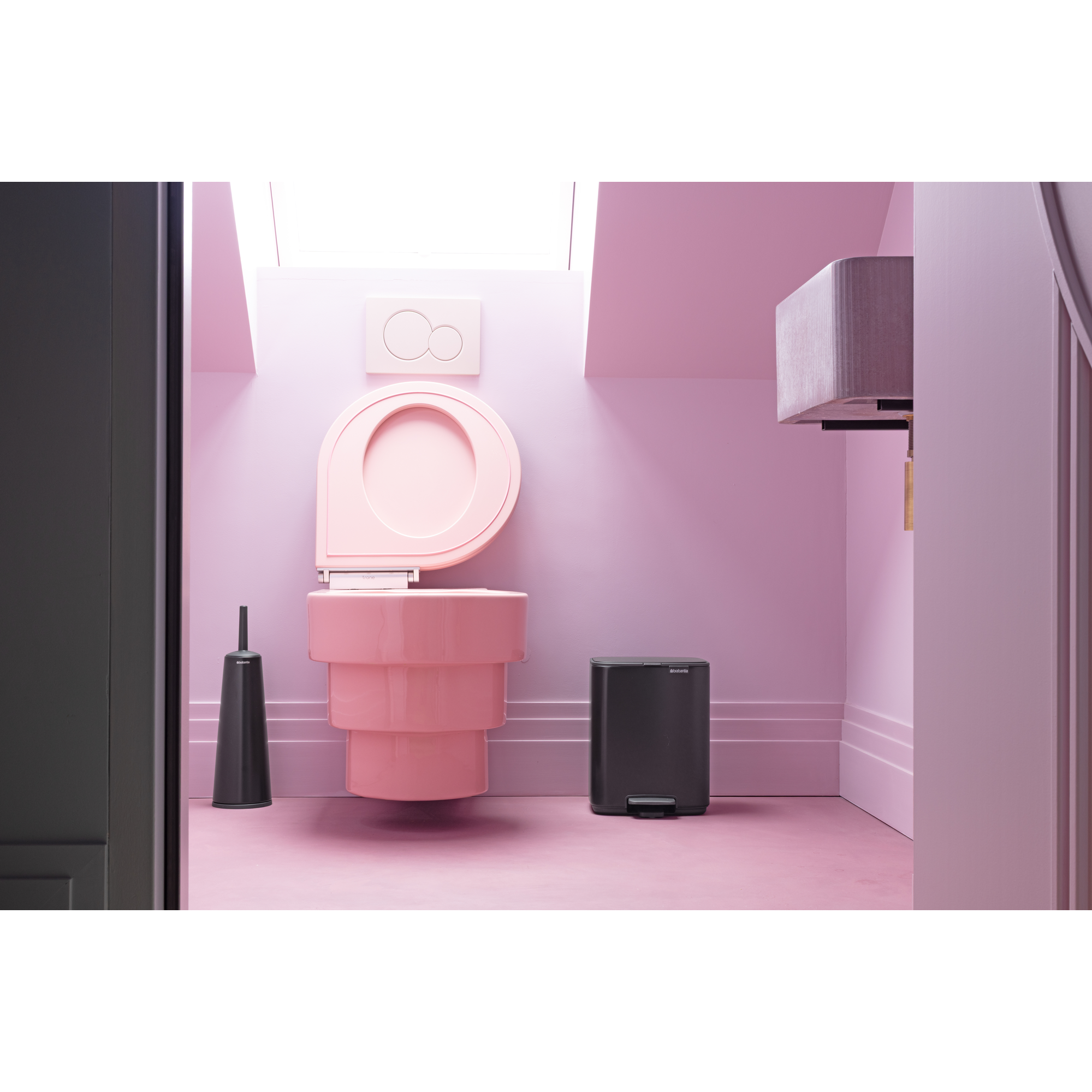 A pink toilet with cistern, brush and bin in a pastel room.