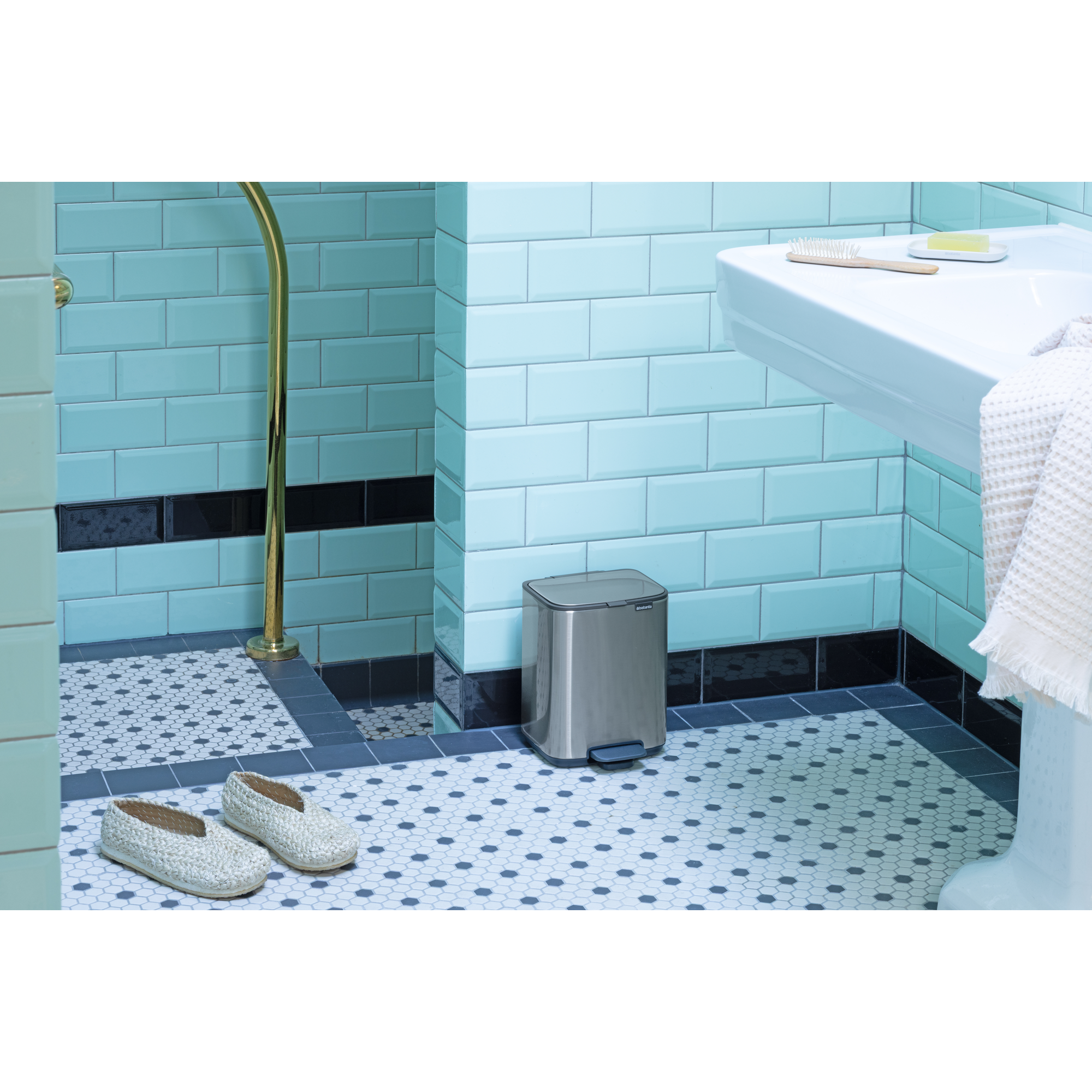 Een badkamer met lichtblauwe tegels, een prullenbak, schoenen en een wastafel.
