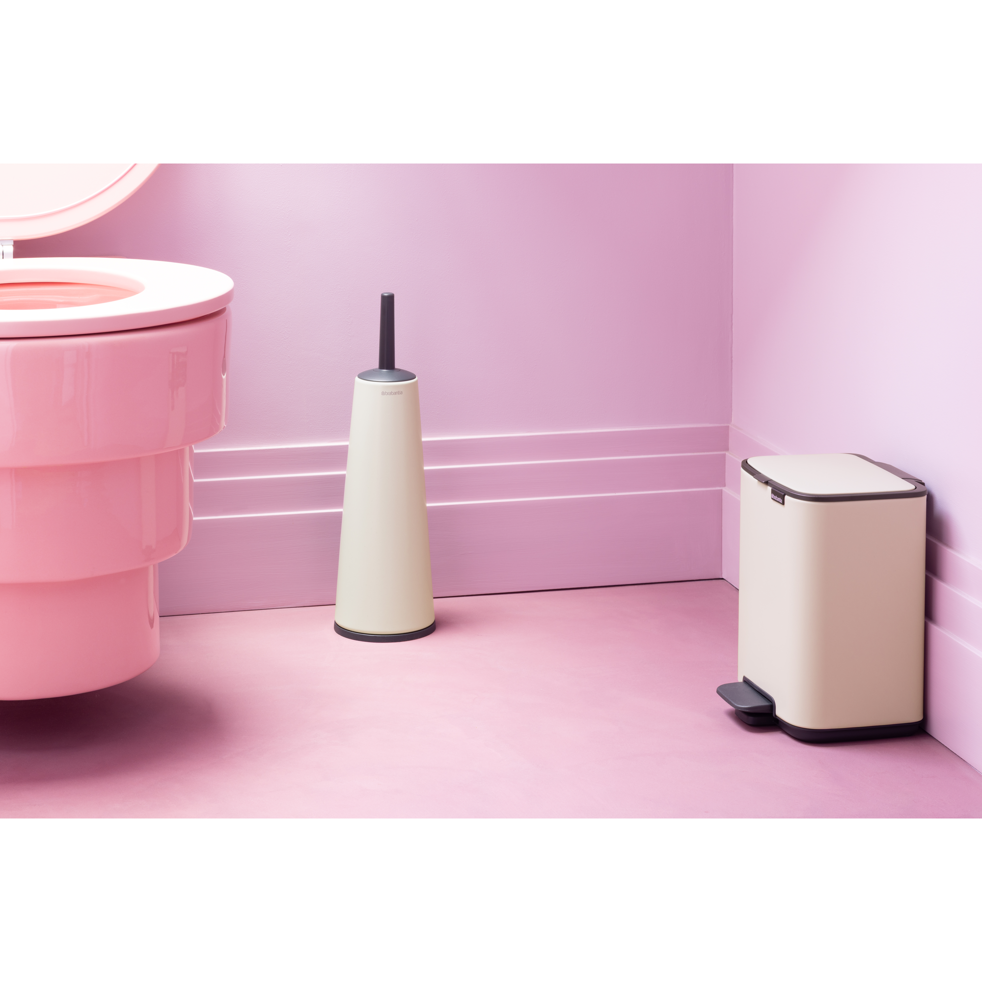 Een roze toilet, een beige borstel en een beige prullenbak op roze vloer.