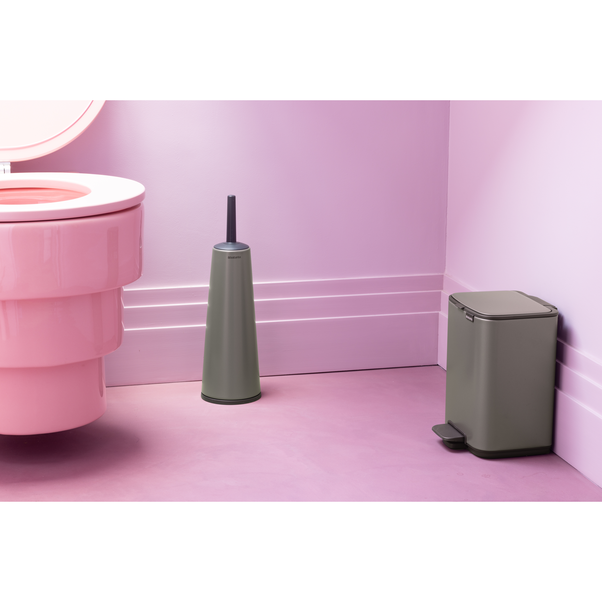 Roze toilet, groene toiletborstel en groene prullenbak op roze vloer.