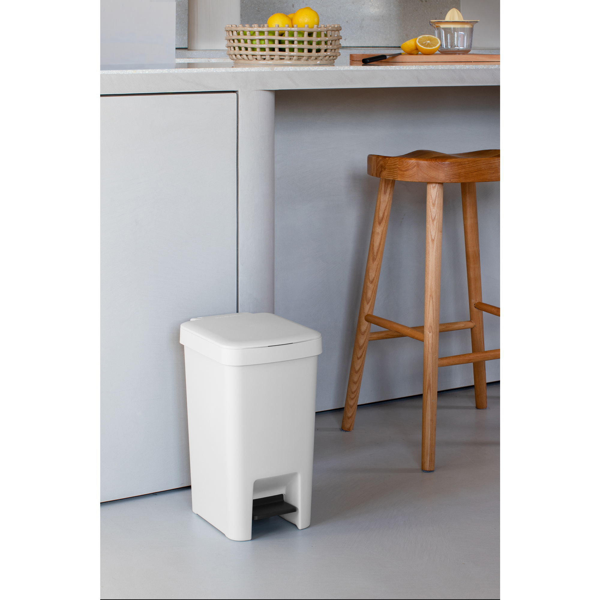 Een witte pedaalemmer staat naast een houten kruk in een keuken.