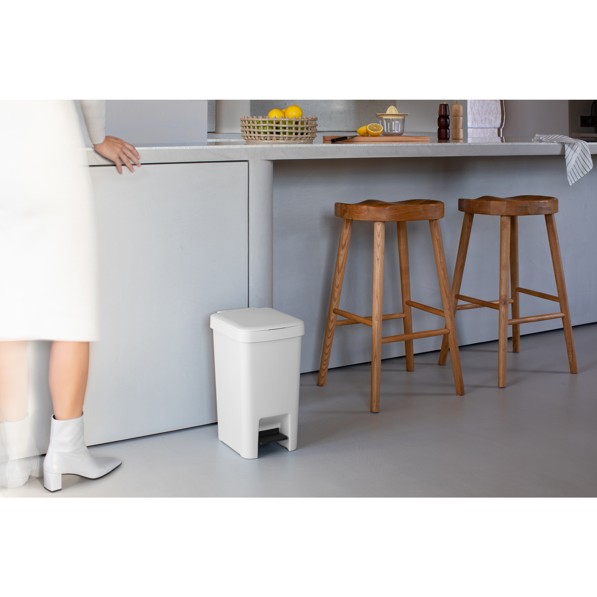 Een witte prullenbak met voetpedaal staat naast twee houten barkrukken.
