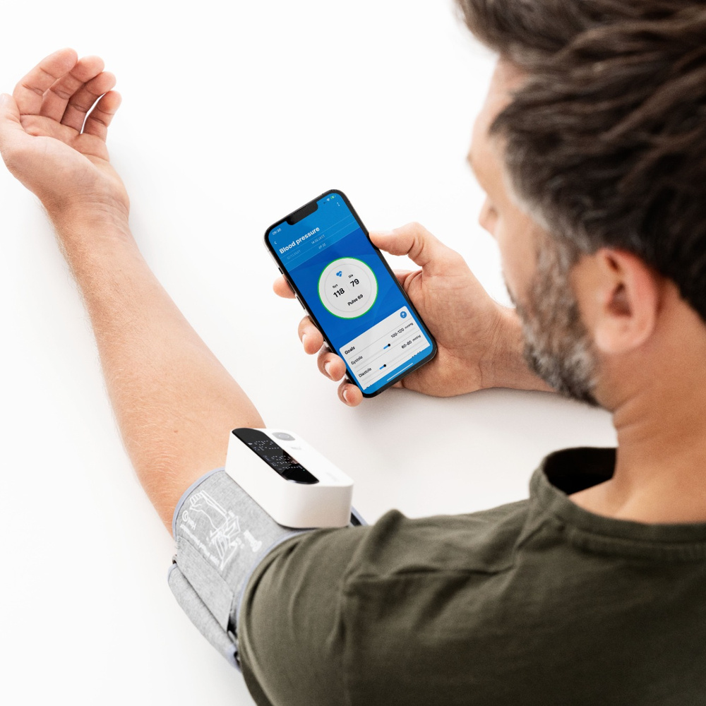 Mann prüft Blutdruck auf Handy-App, verbunden mit Manschette. Werte 118/79.