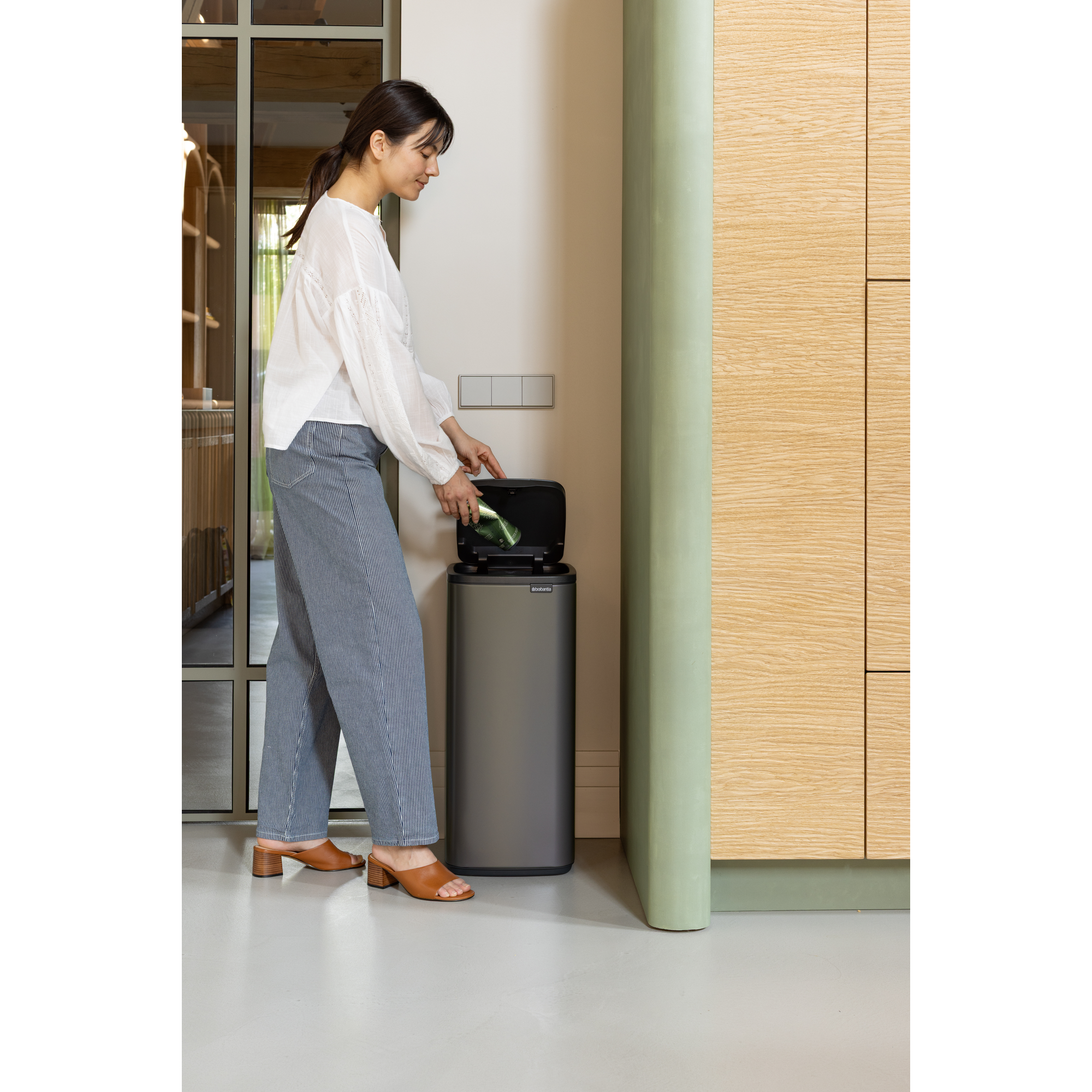 Een vrouw gooit een groene fles in een prullenbak.