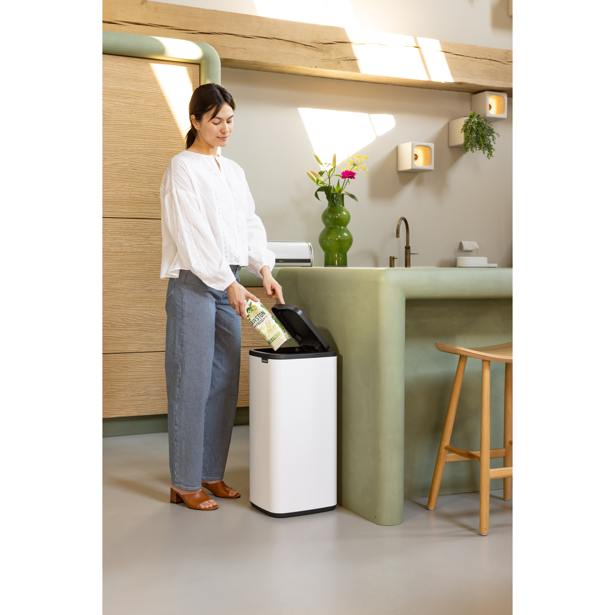 Een vrouw gooit een fles weg in een witte prullenbak in een moderne keuken.