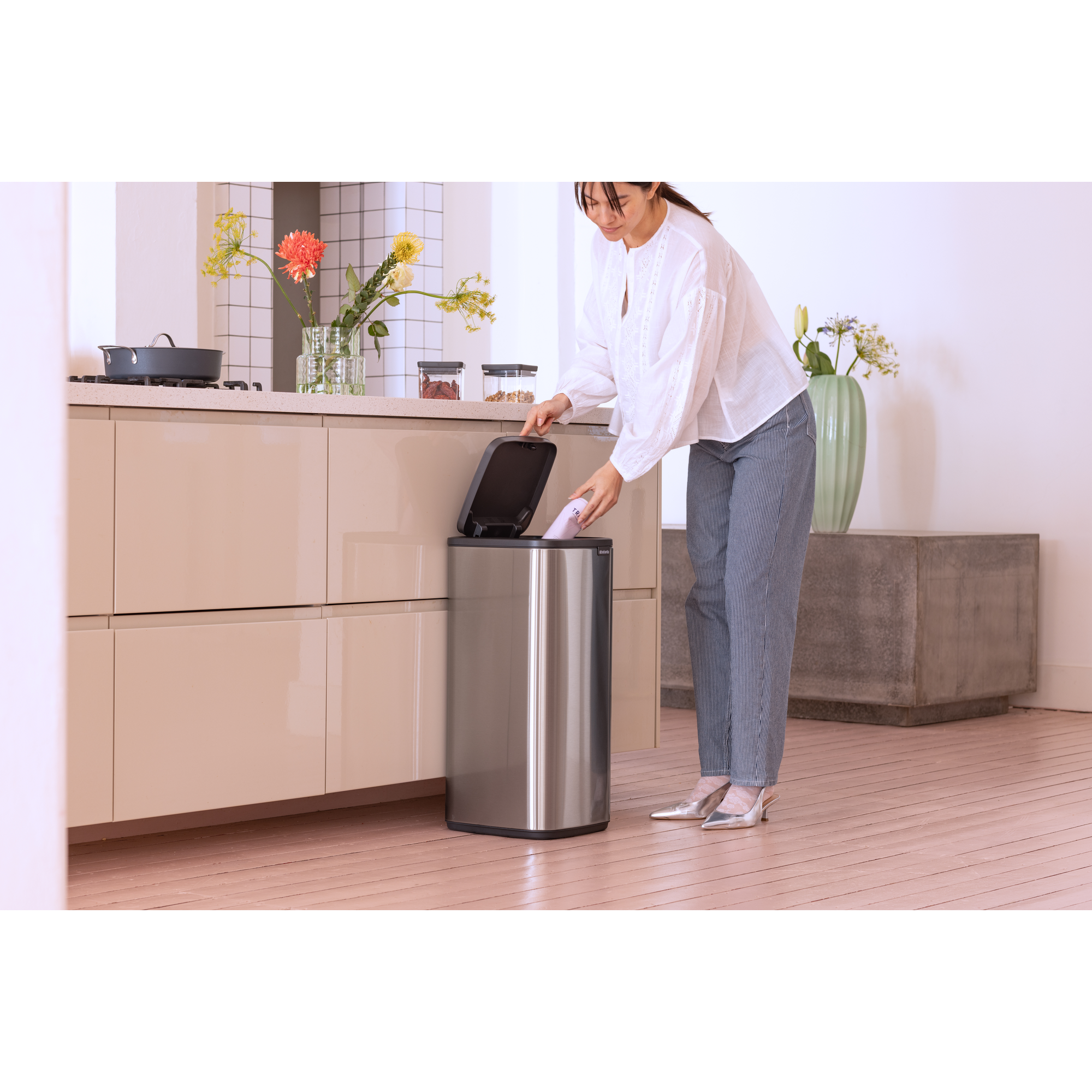 Een vrouw gooit een voorwerp in een zilveren prullenbak in een moderne keuken.