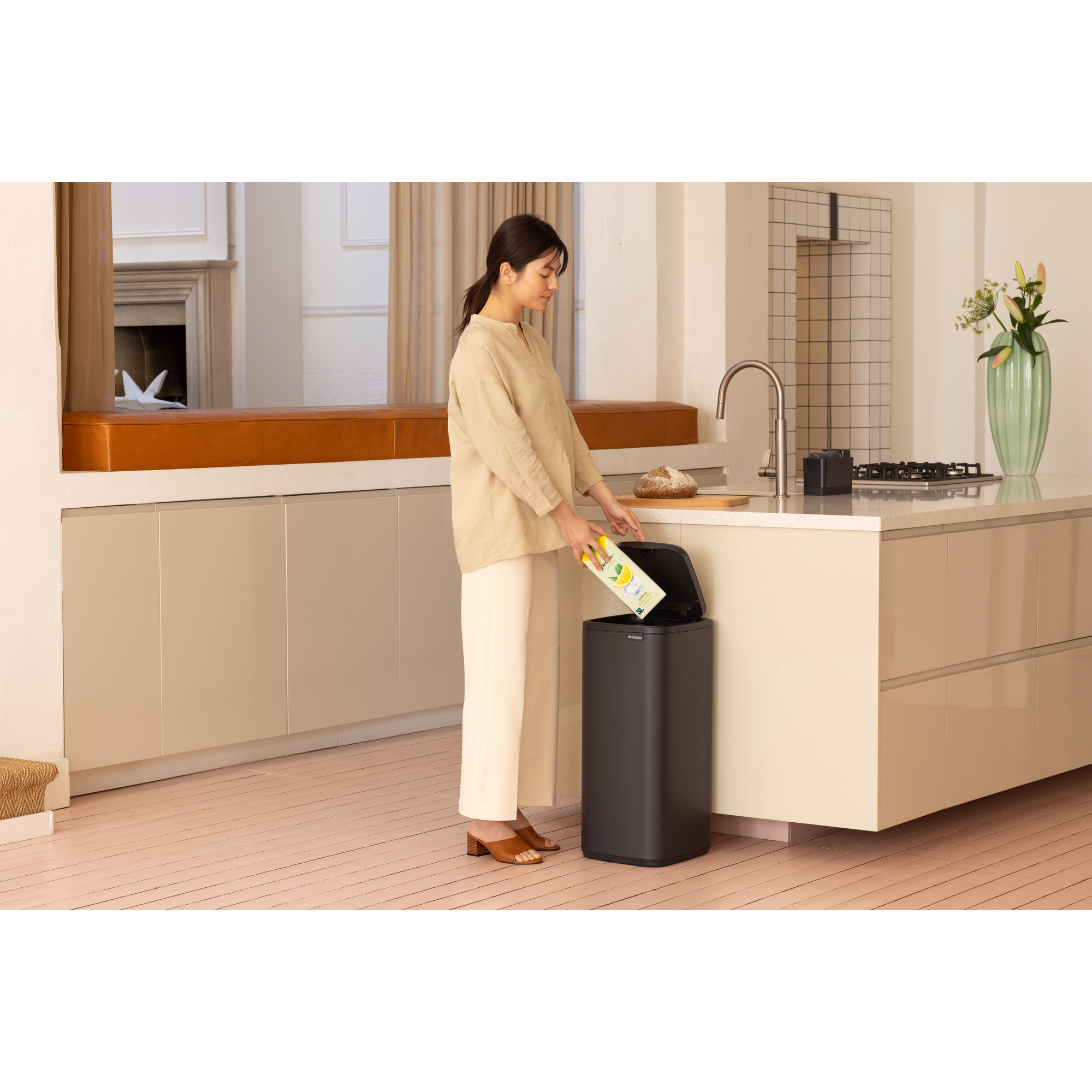 Een vrouw gooit een pak in een donkere prullenbak in een moderne keuken.
