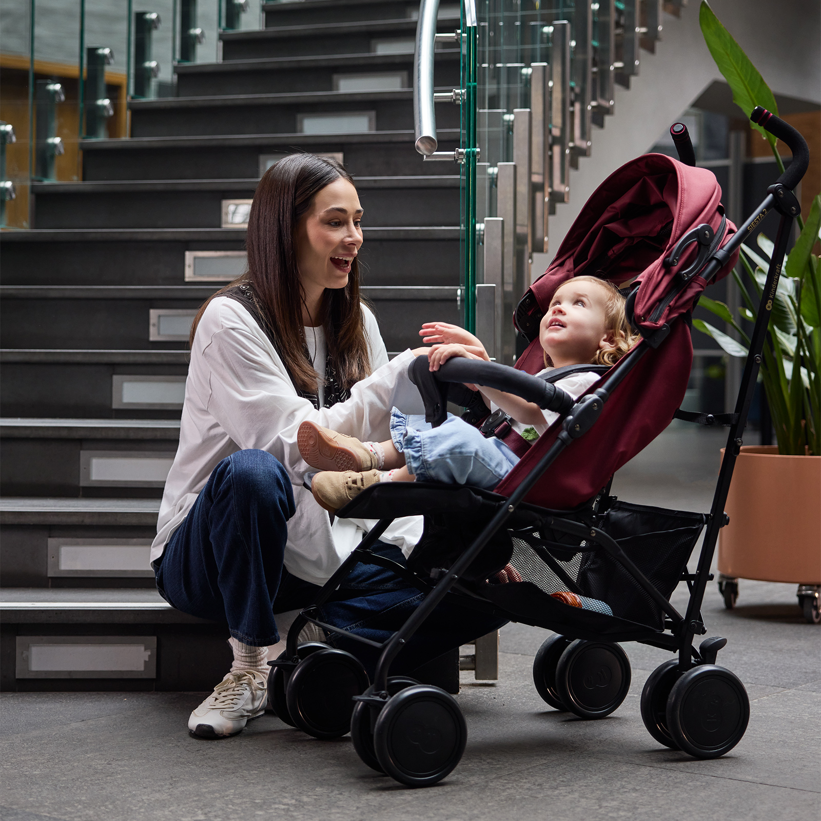 Frau sitzt auf Treppen neben Kinderwagen mit einem Kleinkind.