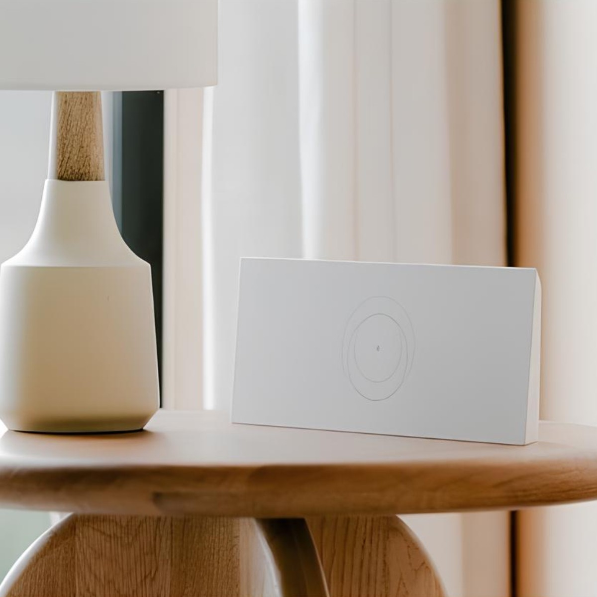 Un orologio digitale bianco minimalista con cerchi concentrici su un tavolo di legno accanto a una lampada.