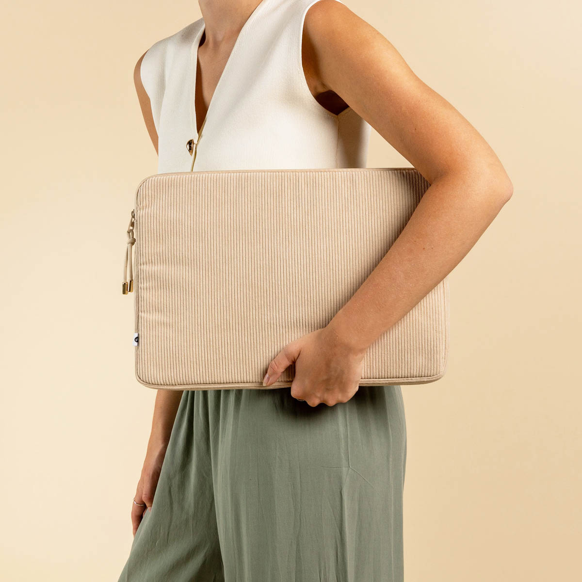 A person holds a beige corduroy laptop sleeve with vertical ribs in front.