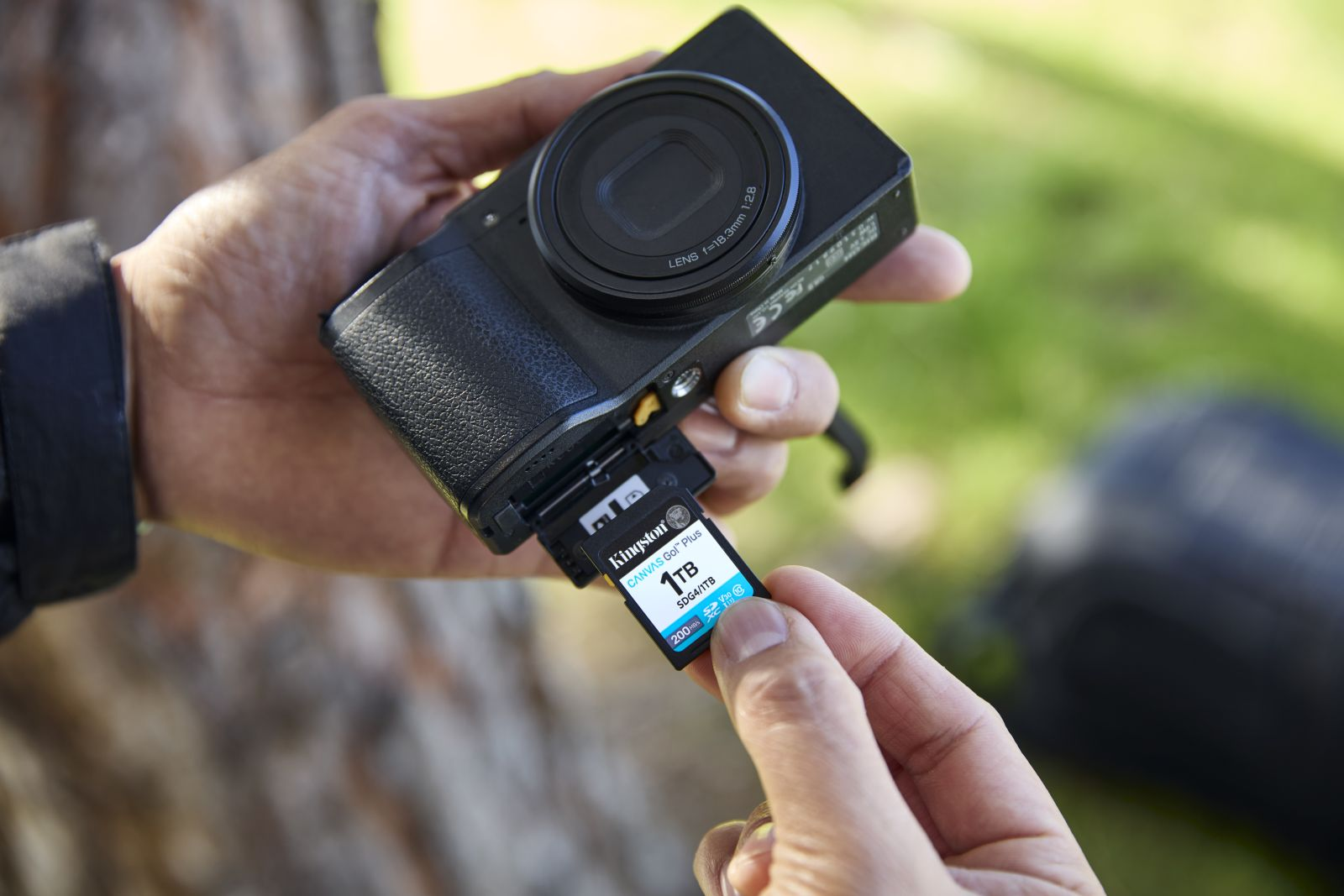 Een hand plaatst een 1TB Kingston SD-kaart in een camera. Wazige achtergrond.