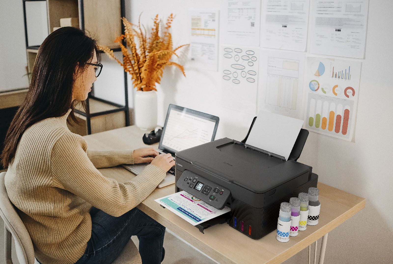 Eine Frau arbeitet an einem Laptop neben einem Drucker mit Tintenflaschen.