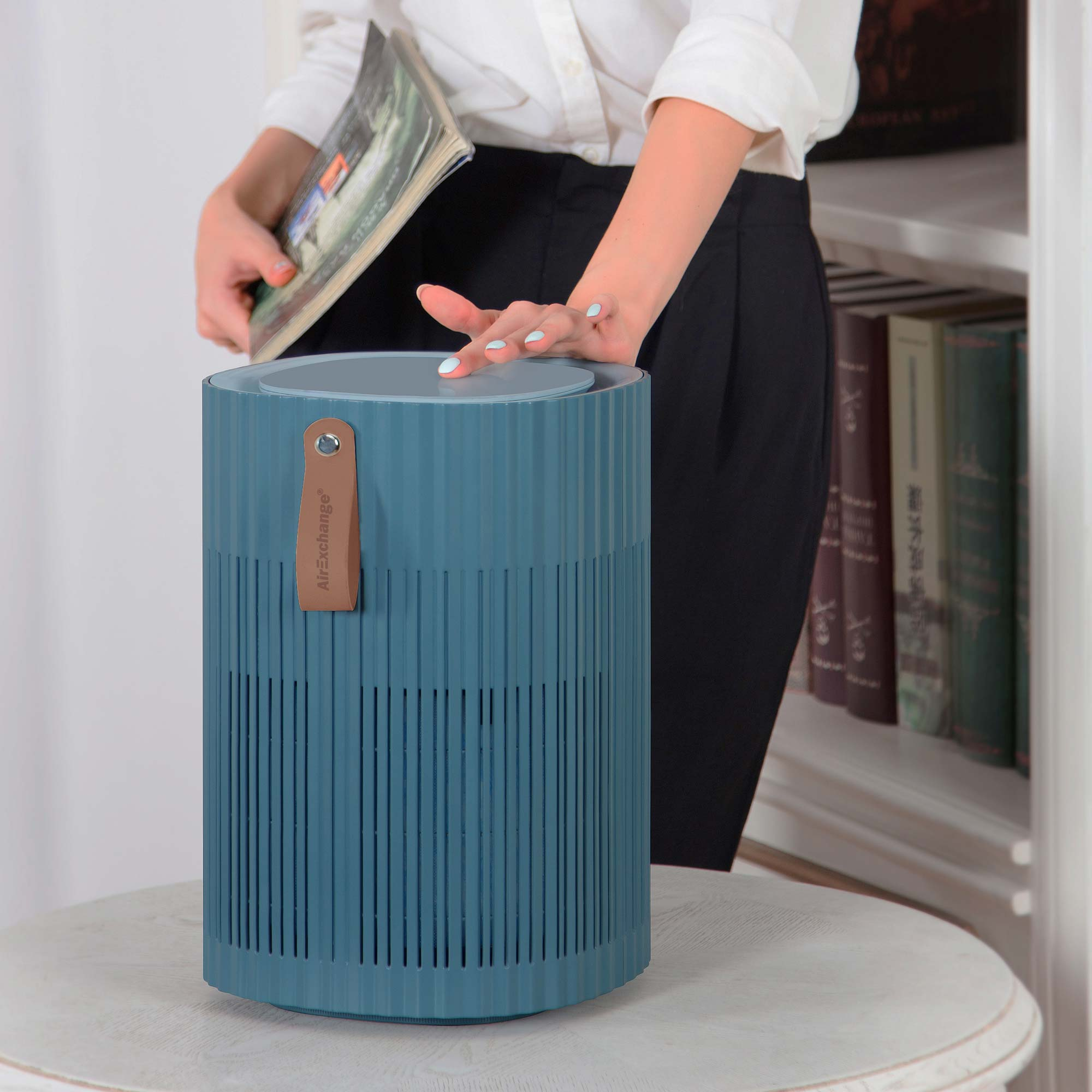 Eine Person mit blauen Nägeln legt ein Buch auf einen blauen Luftreiniger.