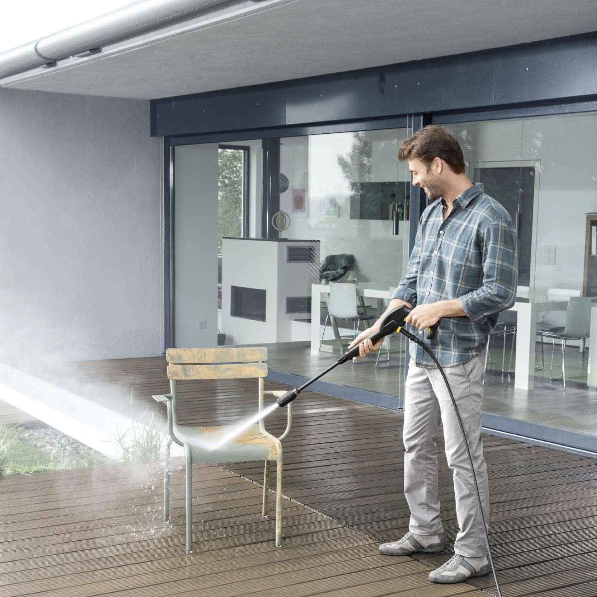 Uomo pulisce sedia arrugginita con idropulitrice su terrazza in legno.