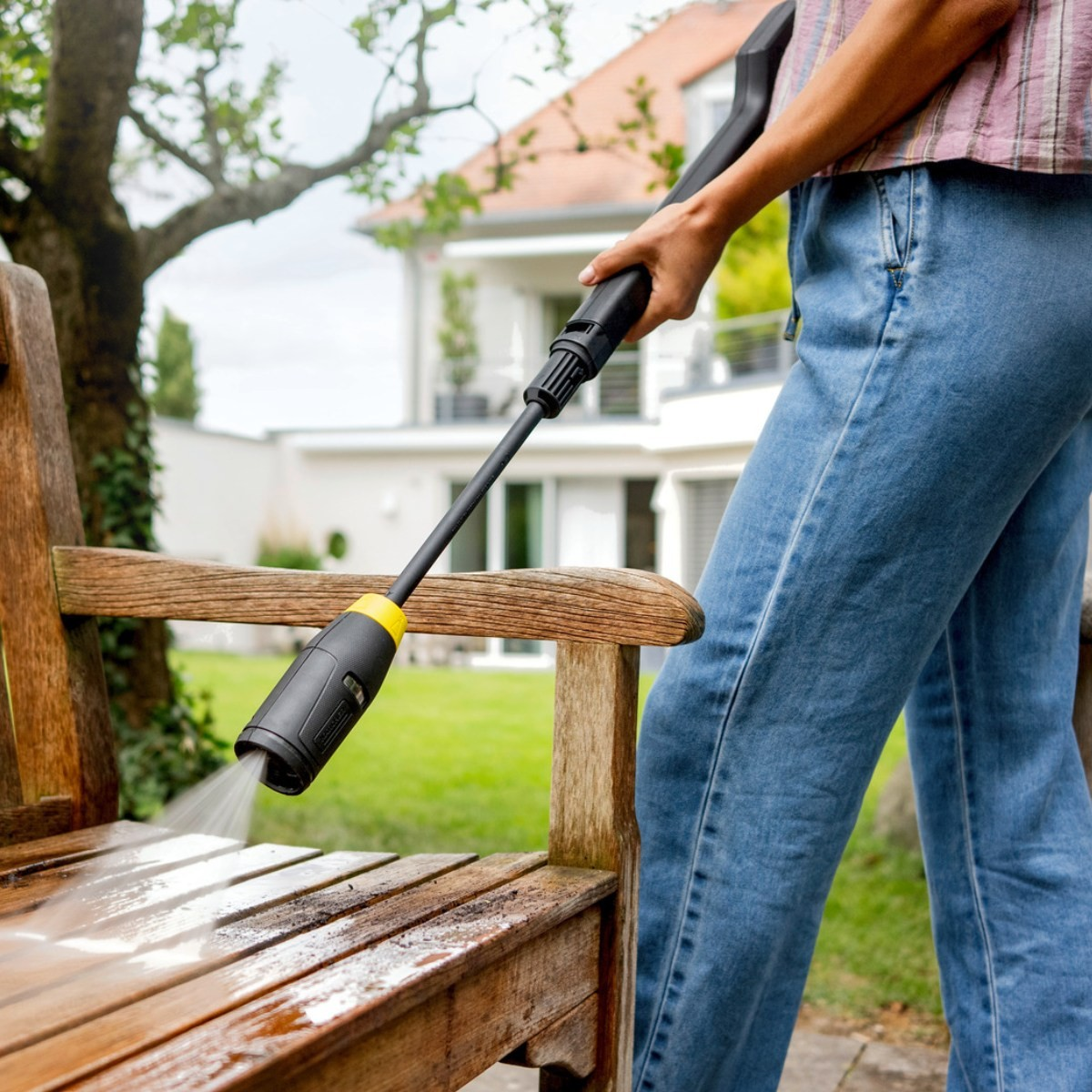 Eine Person reinigt eine Holzbank mit einem Hochdruckreiniger im Garten.