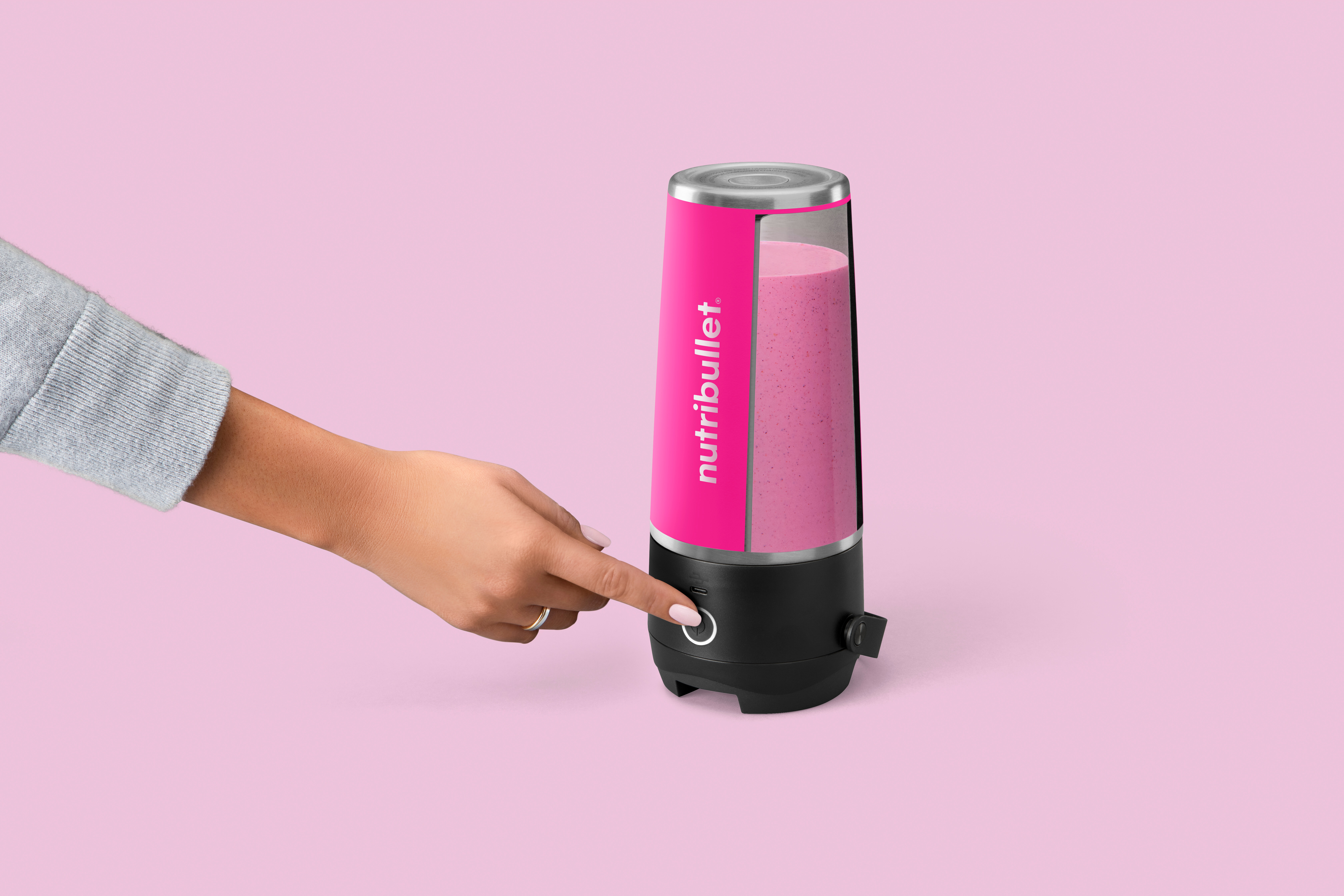 Eine Hand drückt den Knopf eines pinken Nutribullet-Mixers mit pinkem Smoothie.