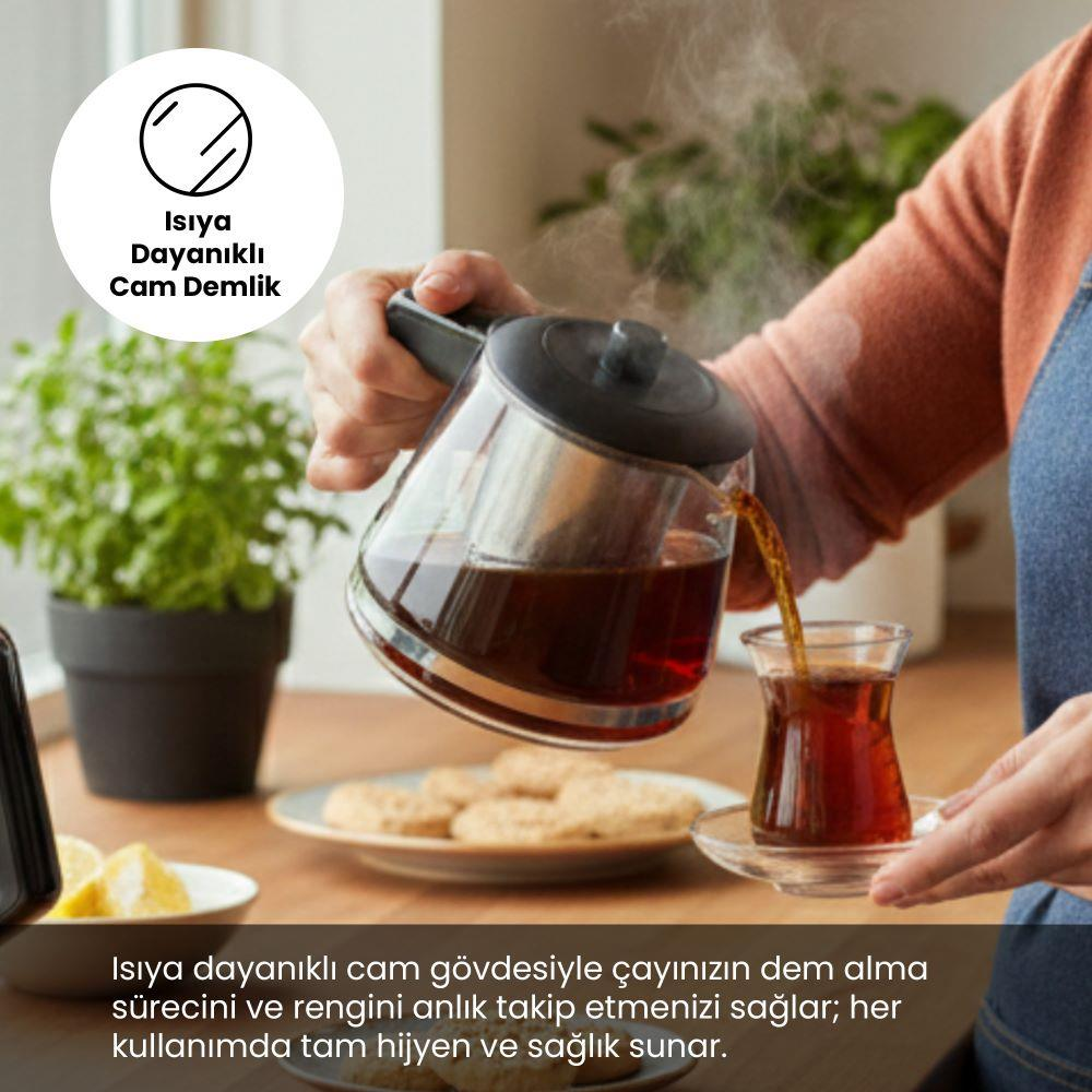 Bir el, cam demlikten bir bardağa sıcak çay döküyor.