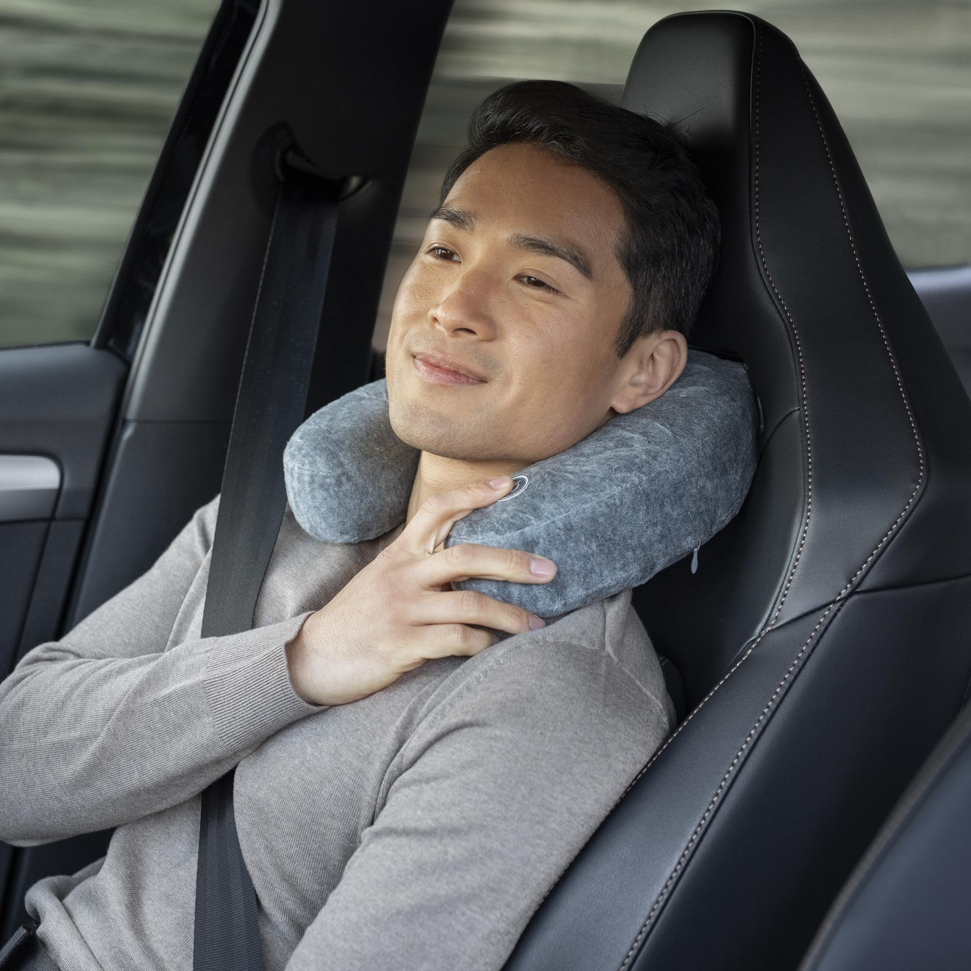 A man wearing a neck pillow in a car, with a seatbelt fastened.