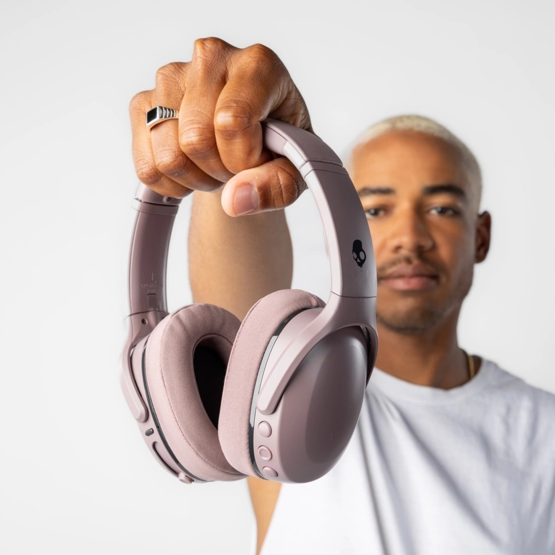 Pembe Skullcandy kulaklık tutan adam. Beyaz arka plan, kulaklığa odaklanma.